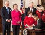 Lilly Ledbetter stands behind President Barack Obama as he signs her namesake law.