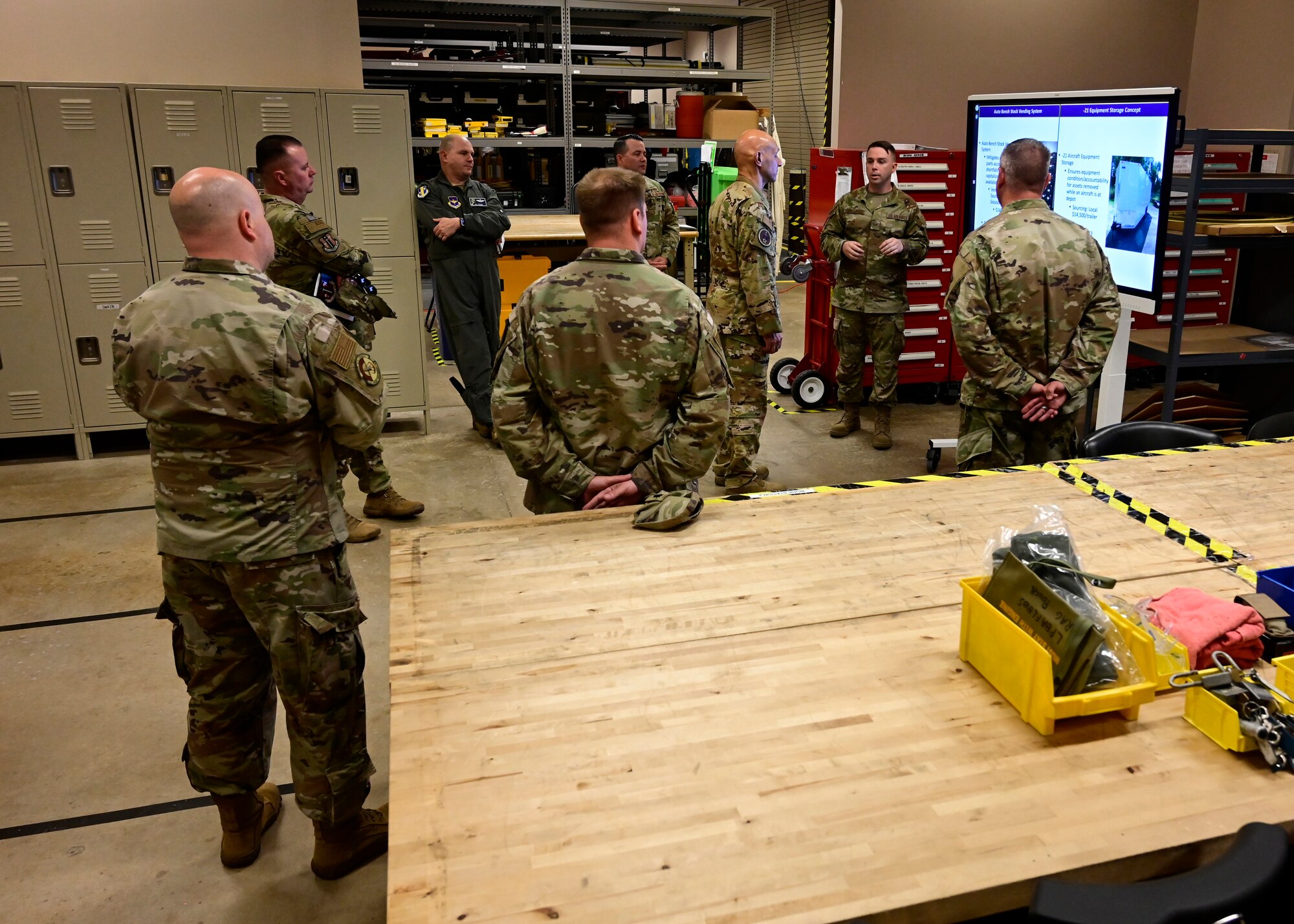 A group of Airmen have a discussion in a room full of tools.