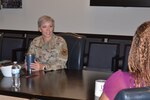 Female military member speaks with civilian employee while sitting at table.
