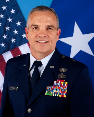 BG Mutchler portrait. Man in US Air Force Uniform smiles in front of flags