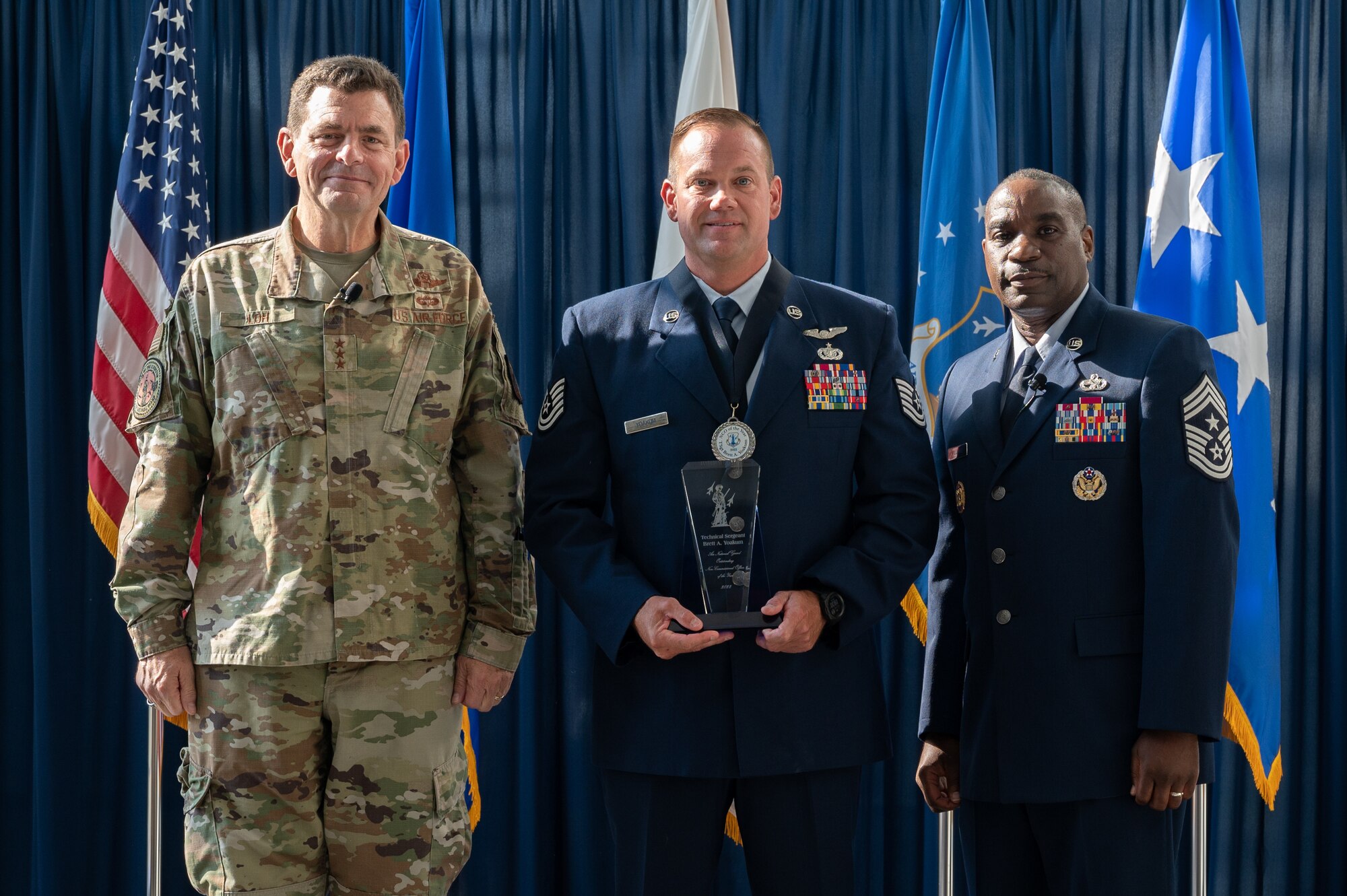 U.S. Air Force Tech Sgt. Brett A. Yoakum, center, of the 164th Airlift Wing, Tennessee National Guard, poses for a photo with Lt. Gen. Michael A. Loh, left, director, Air National Guard (ANG), and Chief Master Sgt. Maurice L. Williams, right, command chief, ANG, during the Outstanding Airmen of the Year ceremony at Joint Base Andrews, Maryland, on Aug. 25, 2022.
