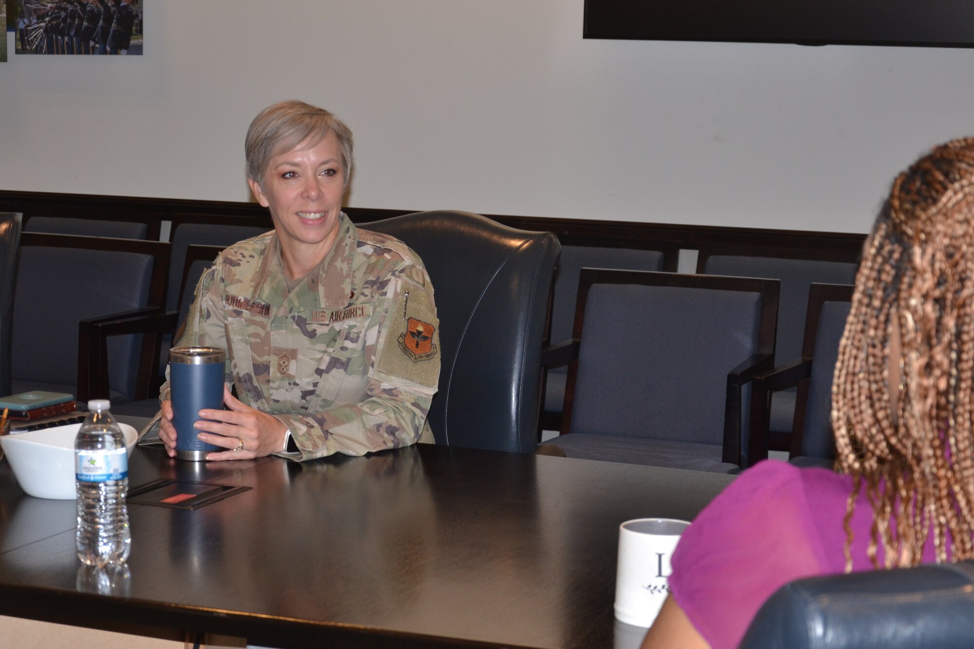 Female military member speaks with civilian employee while sitting at table.