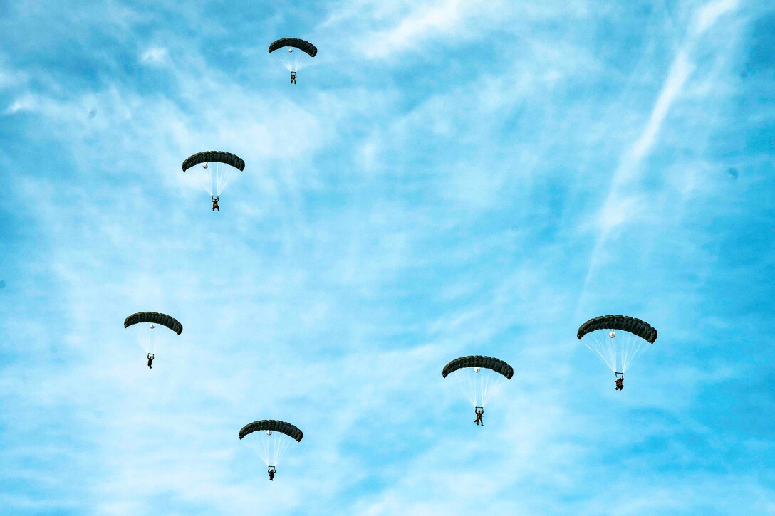 Airmen descend in the sky wearing parachutes.