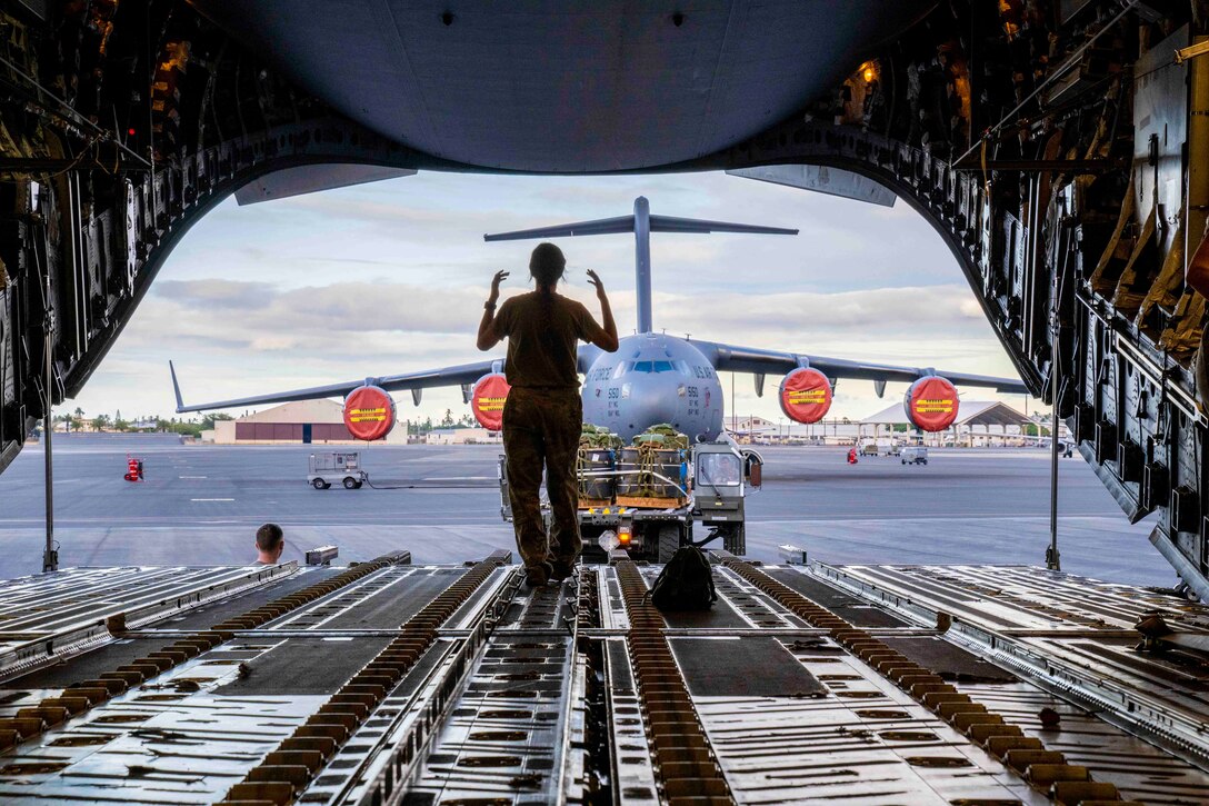 An airman directs a vehicle from the inside of an aircraft.