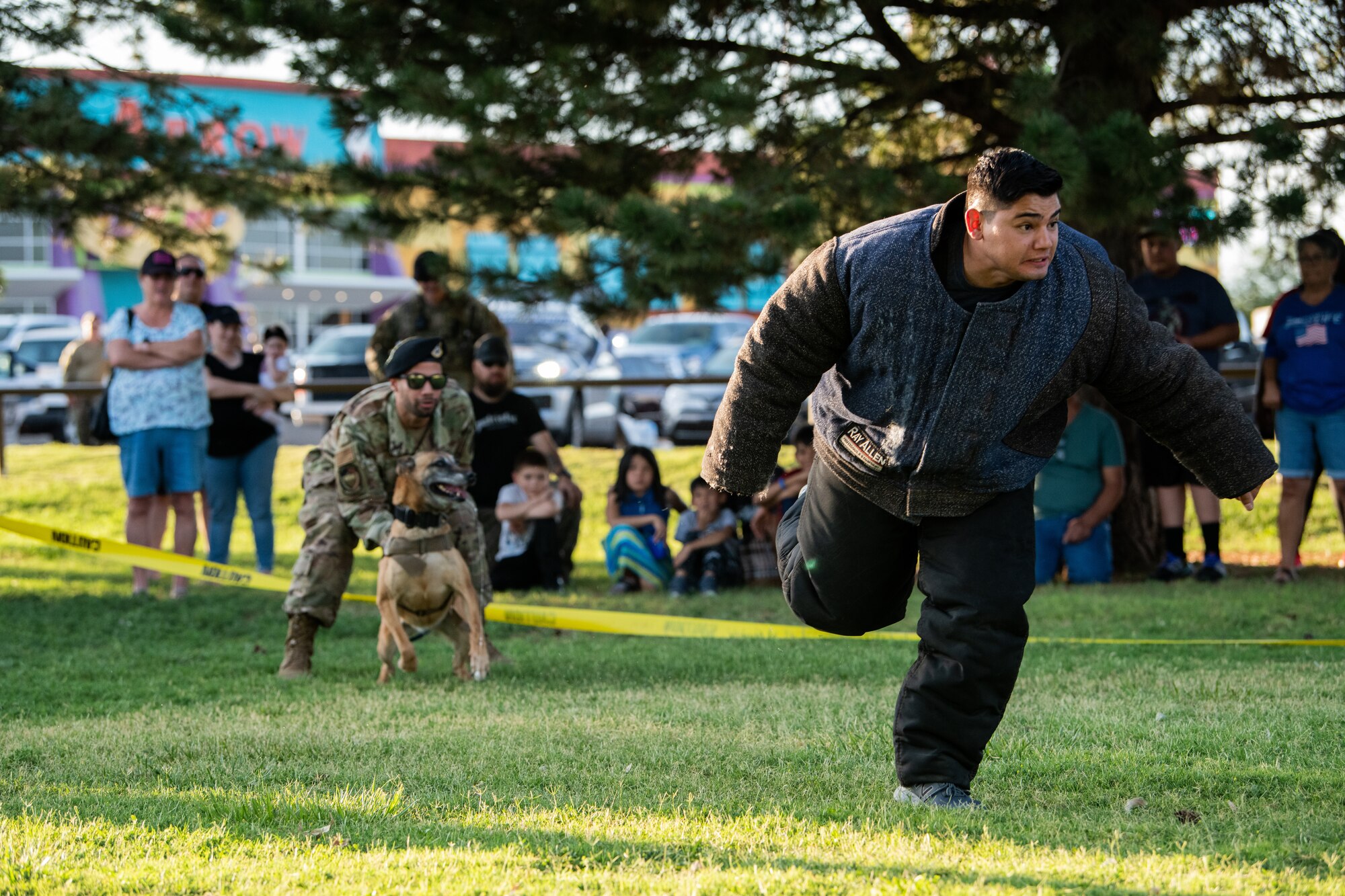 U.S. Air Force Staff Sgt. Johnathan Roman, military working dog Djenga, and Staff Sgt. Leonardo Chico, all assigned to the 27th Special Operations Wing, 27th Special Operations Security Forces Squadron, Cannon Air Force Base, demonstrate a fleeing suspect chase scenario for Clovis residents during National Night Out Aug. 2, 2022, at Green Acres Park, Clovis, New Mexico. Cannon Air Commandos from the 27th SOSFS and various New Mexico law enforcement and first responders took part in the event, which is part of a nation-wide campaign to strengthen community safety and enhance relationships between residents and law enforcement. (U.S. Air Force photo by Staff Sgt. Peter Reft)