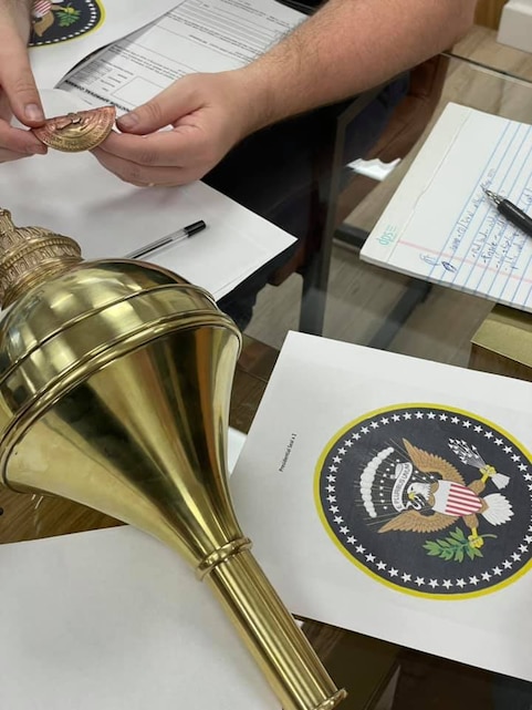 A blank mace globe rests on a table next to a detailed printout of the presidential seal. Photo taken during Drum Major Master Gunnery Sgt. King's September 2021 visit to mace manufacturing company Dalman & Narborough, based in Birmingham, England. Courtesy of Dalman & Narborough.