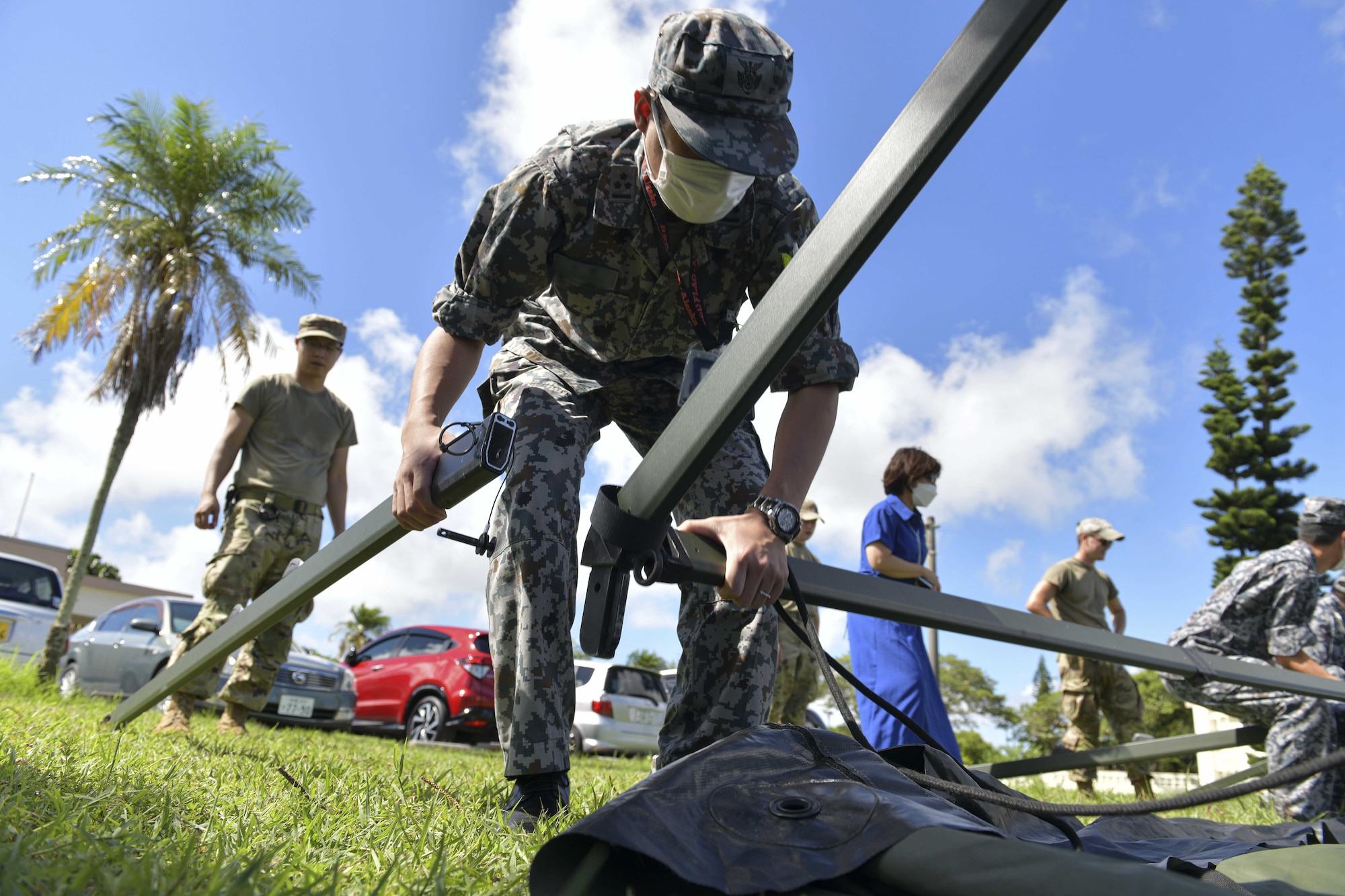 A Japanese military member sets up the leg of a tent under the supervision of U.S. military instructors