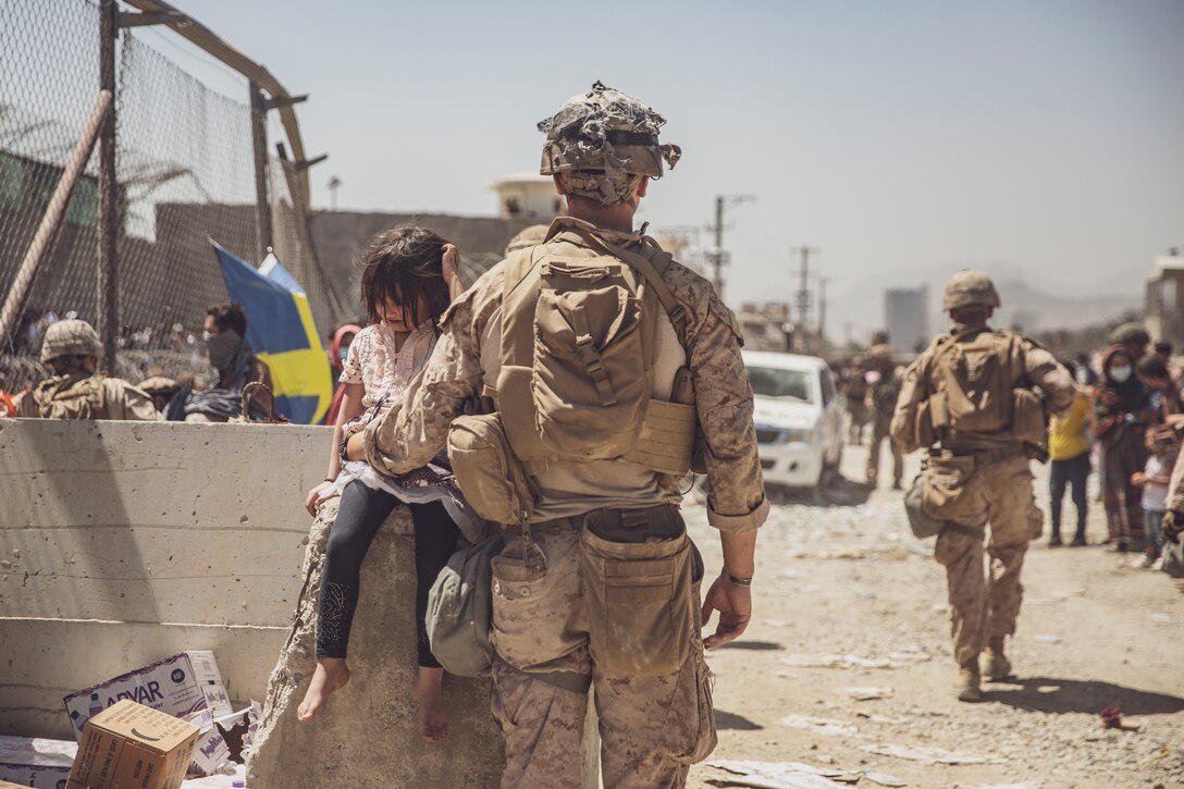 A U.S. Marine with Special Purpose Marine Air-Ground Task Force - Crisis Response - Central Command takes care of a young girl awaiting processing at an Evacuation Control Checkpoint (ECC) during an evacuation at Hamid Karzai International Airport, Kabul, Afghanistan, Aug. 26, 2021.