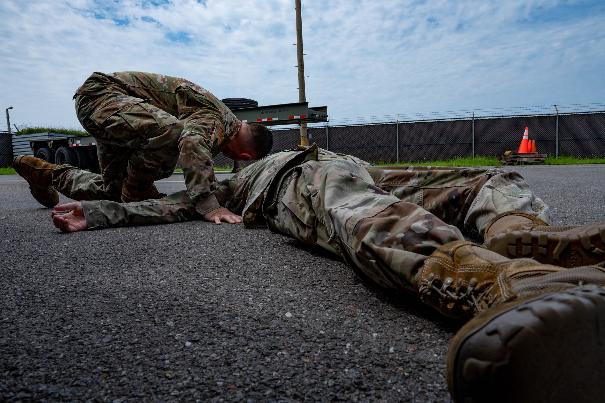 Airman lies on a ground during simulated medical event while another Airman assists by providing aide.