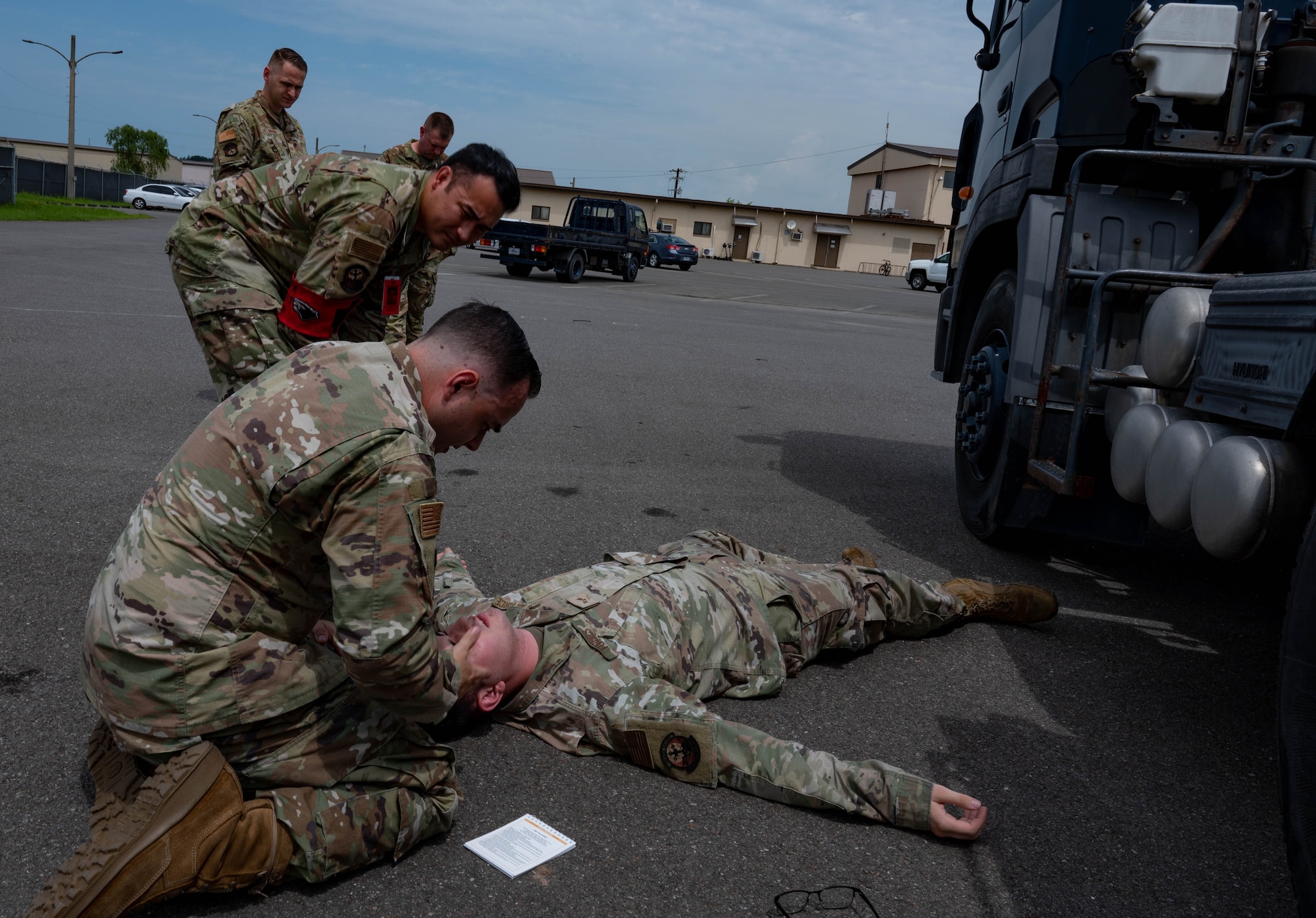 Airman lies on a ground during simulated medical event while another Airman assists by providing aide.