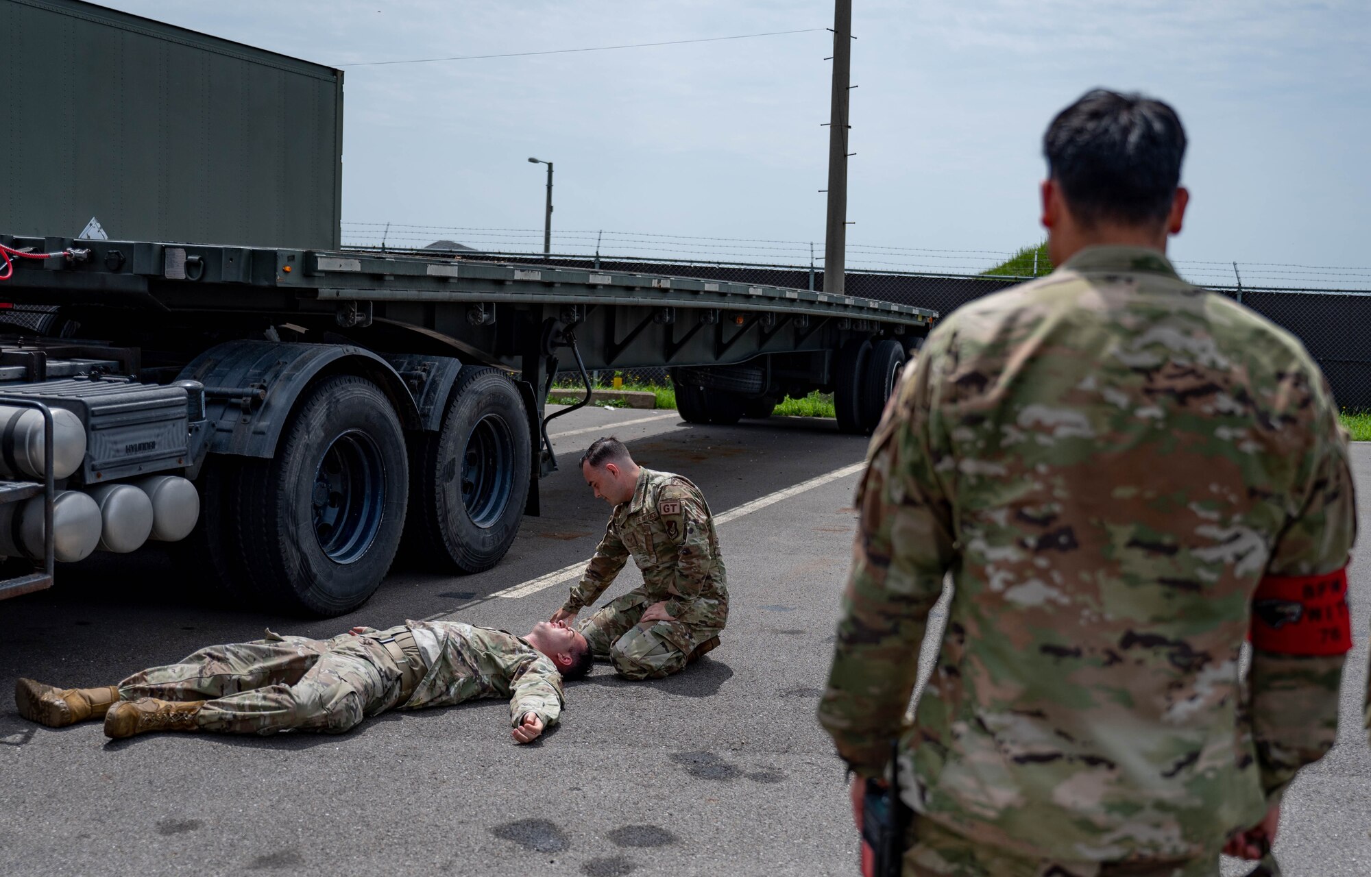 Airman lies on a ground during simulated medical event while another Airman assists by providing aide.