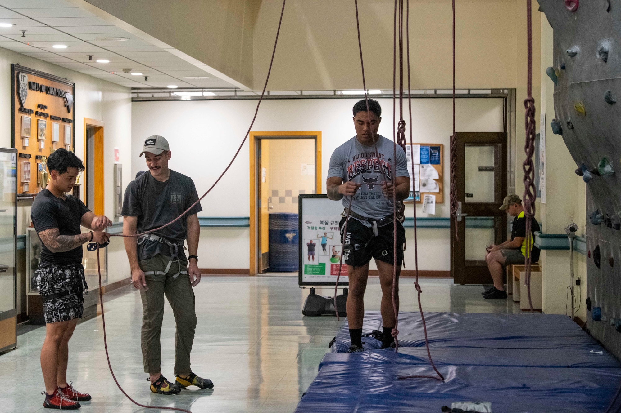 U.S. Air Force Staff Sgt. Reynaldo Tamayo (right), 8th Medical Group systems administrator, hooks up a belay as Staff Sgt. Emilio Perales (center), 35th Fighter Generation Squadron dedicated crew chief and gym climbing instructor, watches and a student climber harnesses in at Kunsan Air Base, Republic of Korea, Aug. 23, 2022. The Wolf Pack Fitness Center holds the class every Tuesday at 6 p.m. and teaches Airmen to safely belay, use climbing commands and harness in. (U.S. Air Force photo by Staff Sgt. Sadie Colbert)