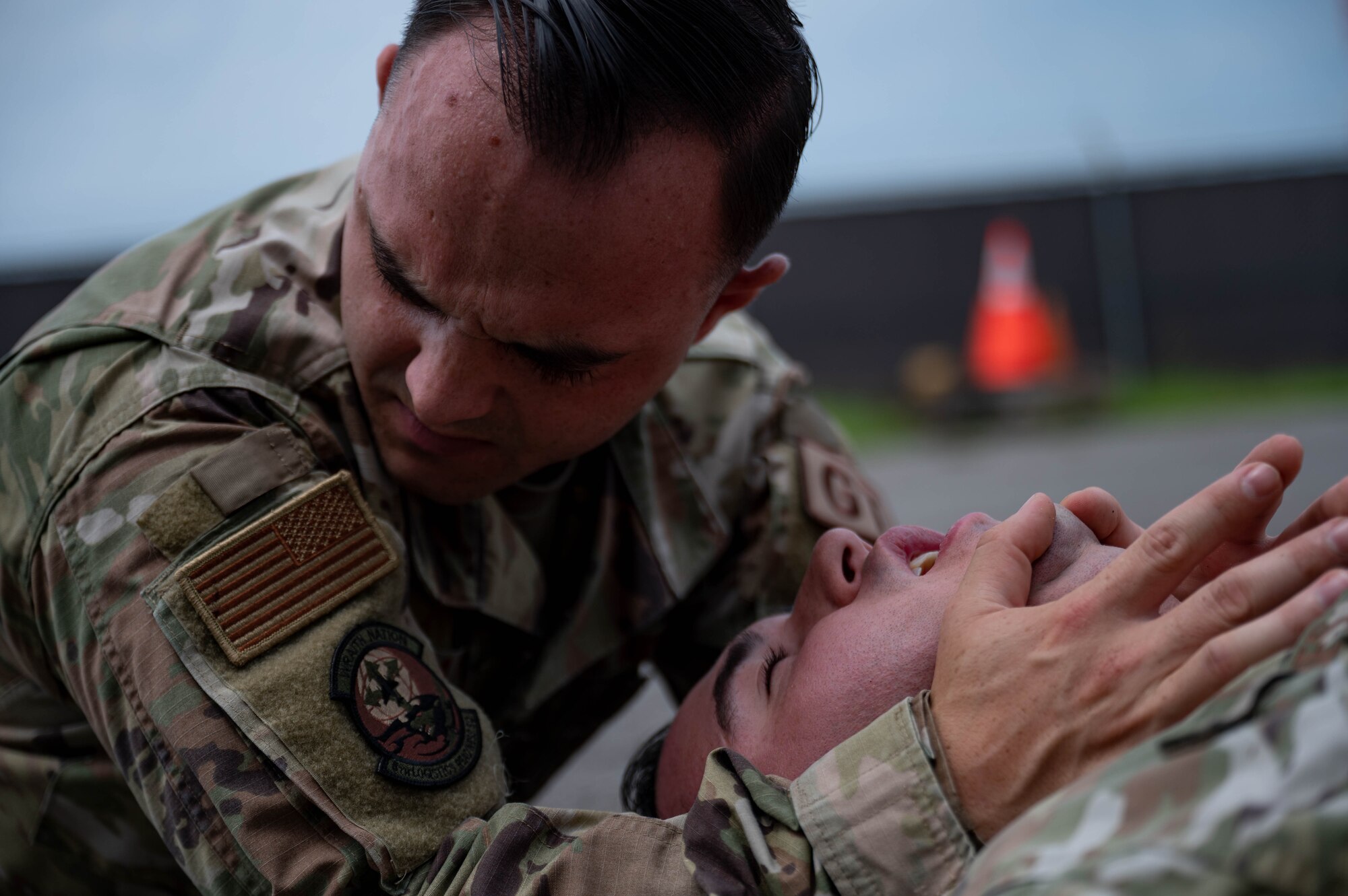 Airman lies on a ground during simulated medical event while another Airman assists by providing aide.