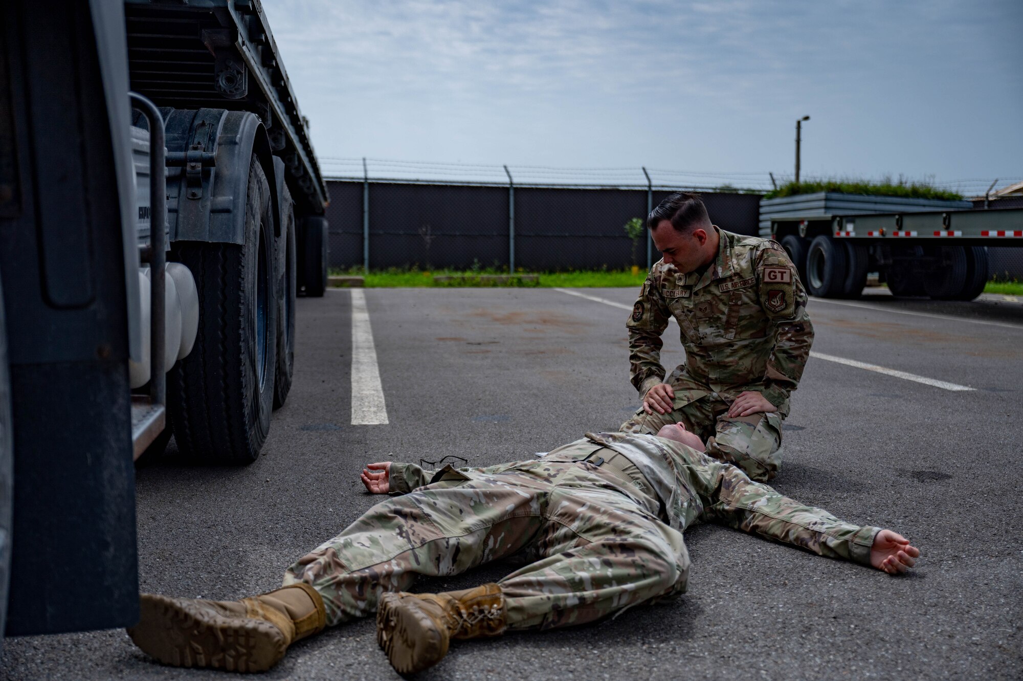 Airman lies on a ground during simulated medical event while another Airman assists by providing aide.