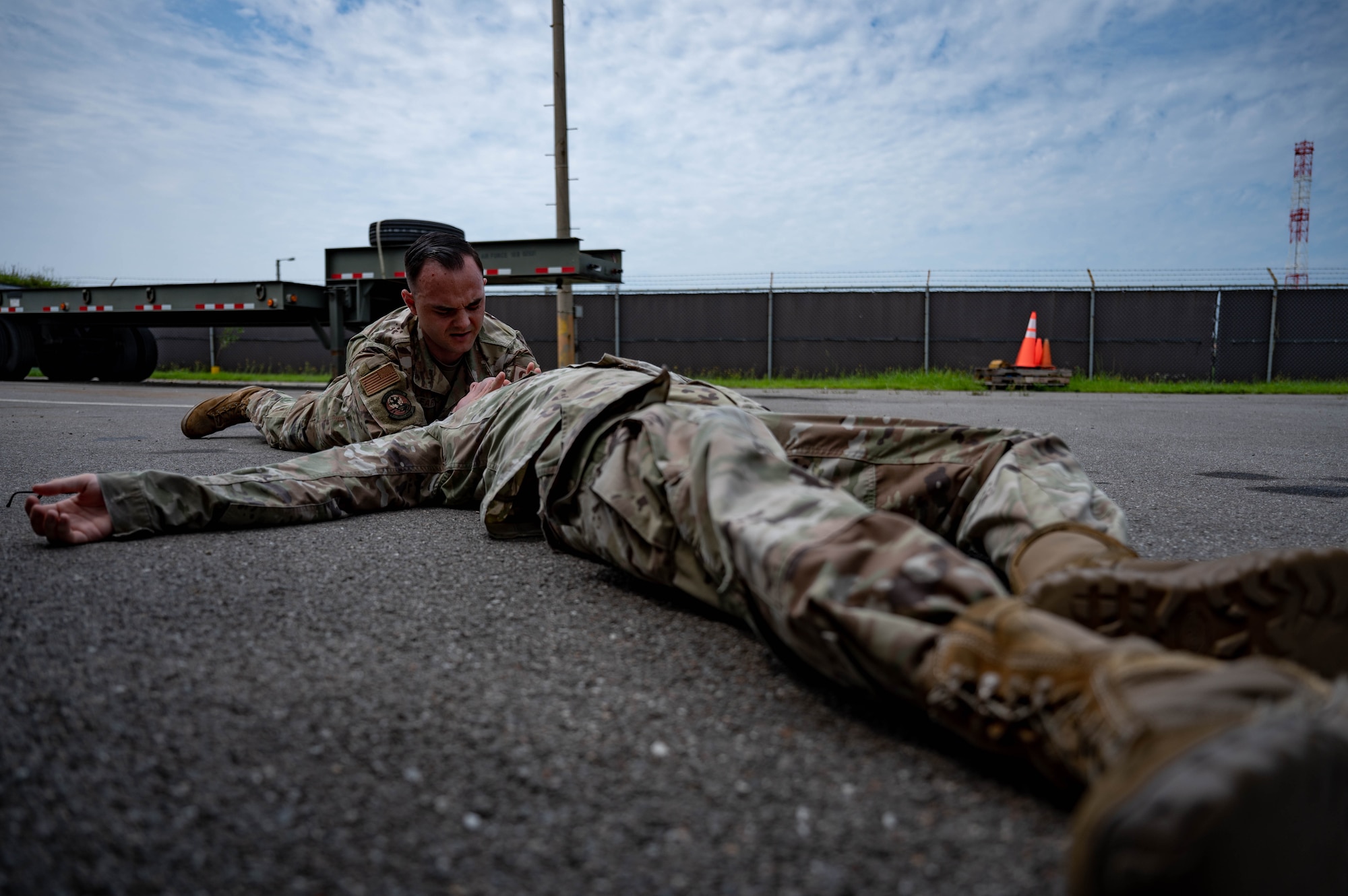 Airman lies on a ground during simulated medical event while another Airman assists by providing aide.