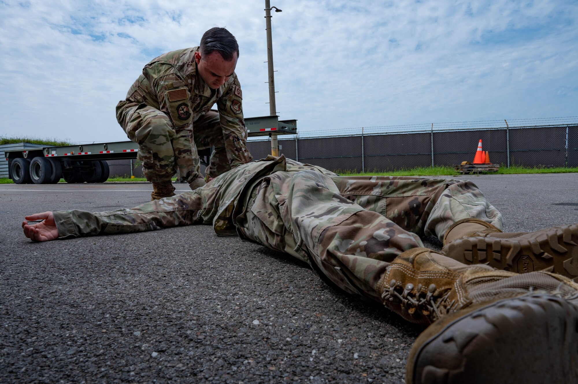Airman lies on a ground during simulated medical event while another Airman assists by providing aide.