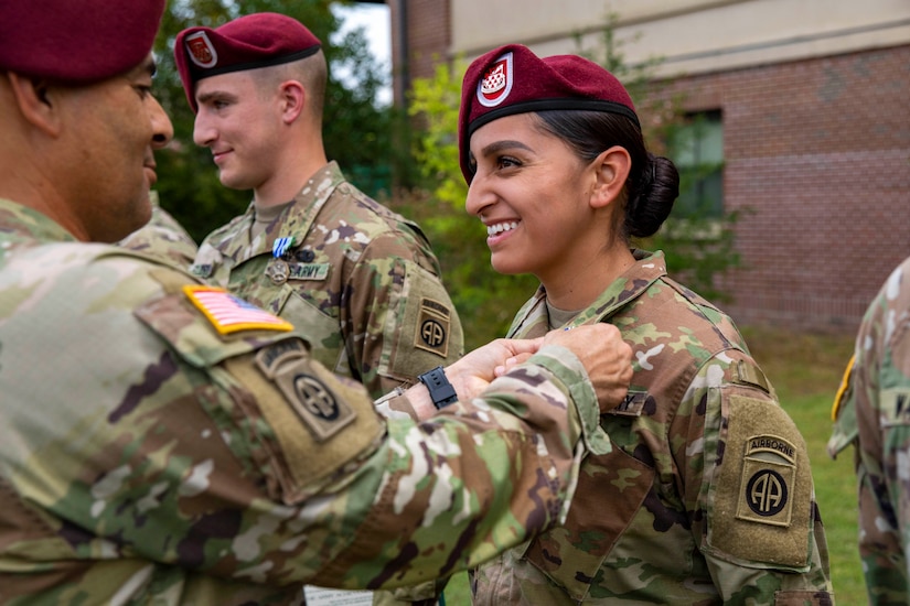 A soldier standing in a line receives a pin on her uniform’s collar from a commanding soldier.