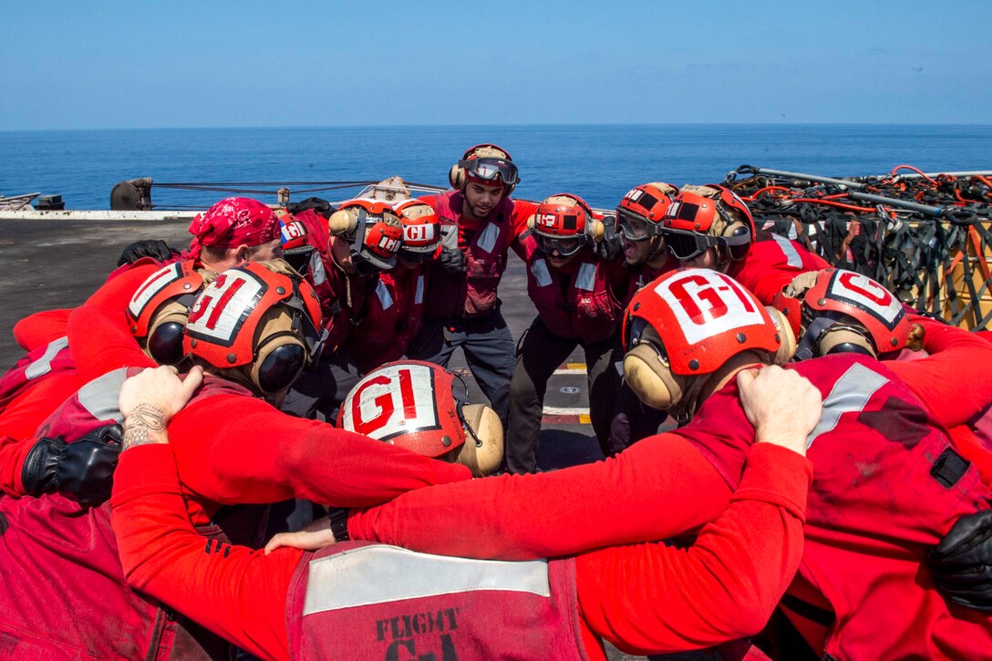 A group of sailors huddle on the deck of a ship.