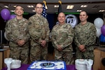 Four military men in uniform pose for a photo in front of a cake