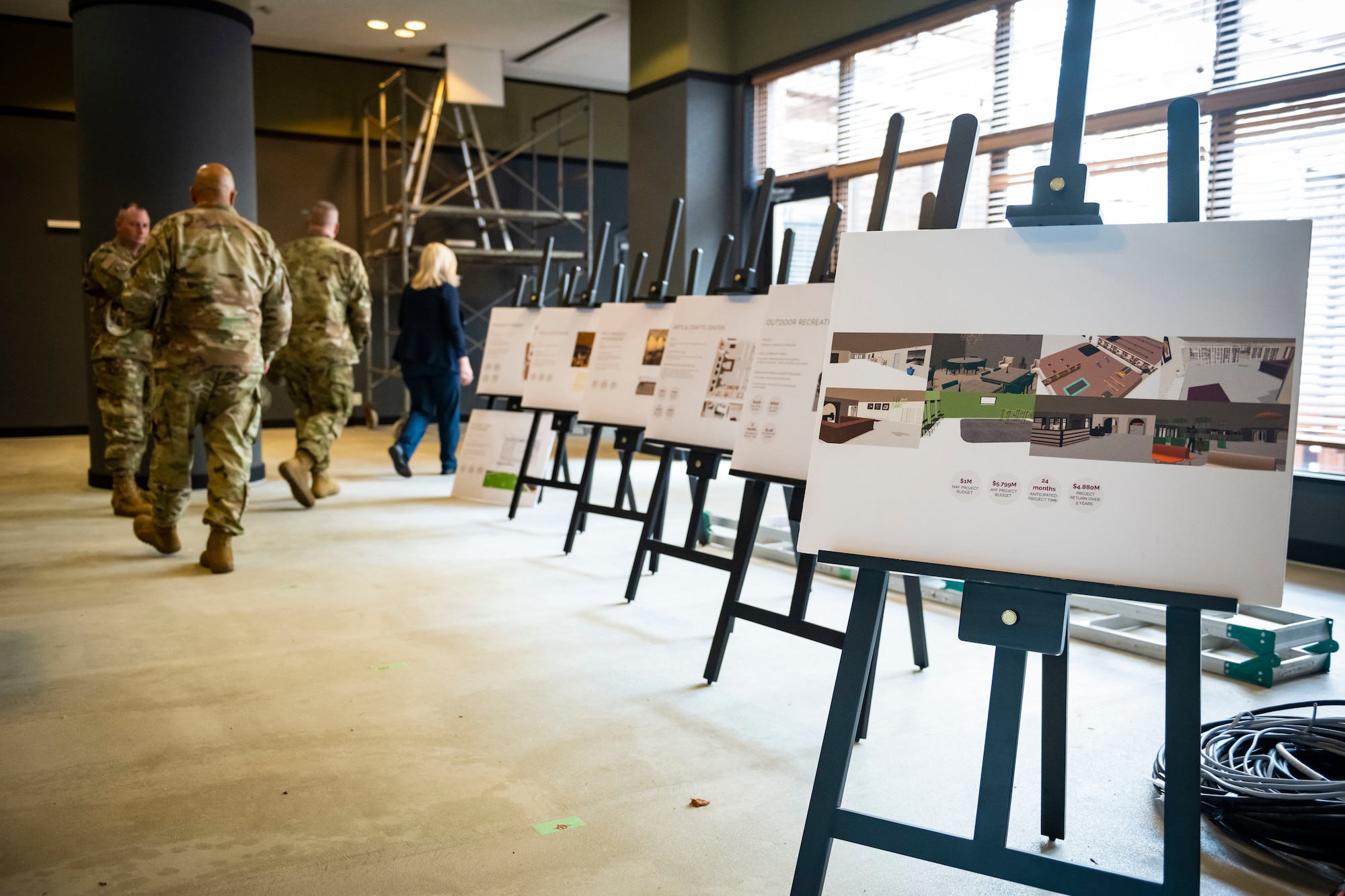 Billboards are displayed on stands as U.S. military members walk in the background.