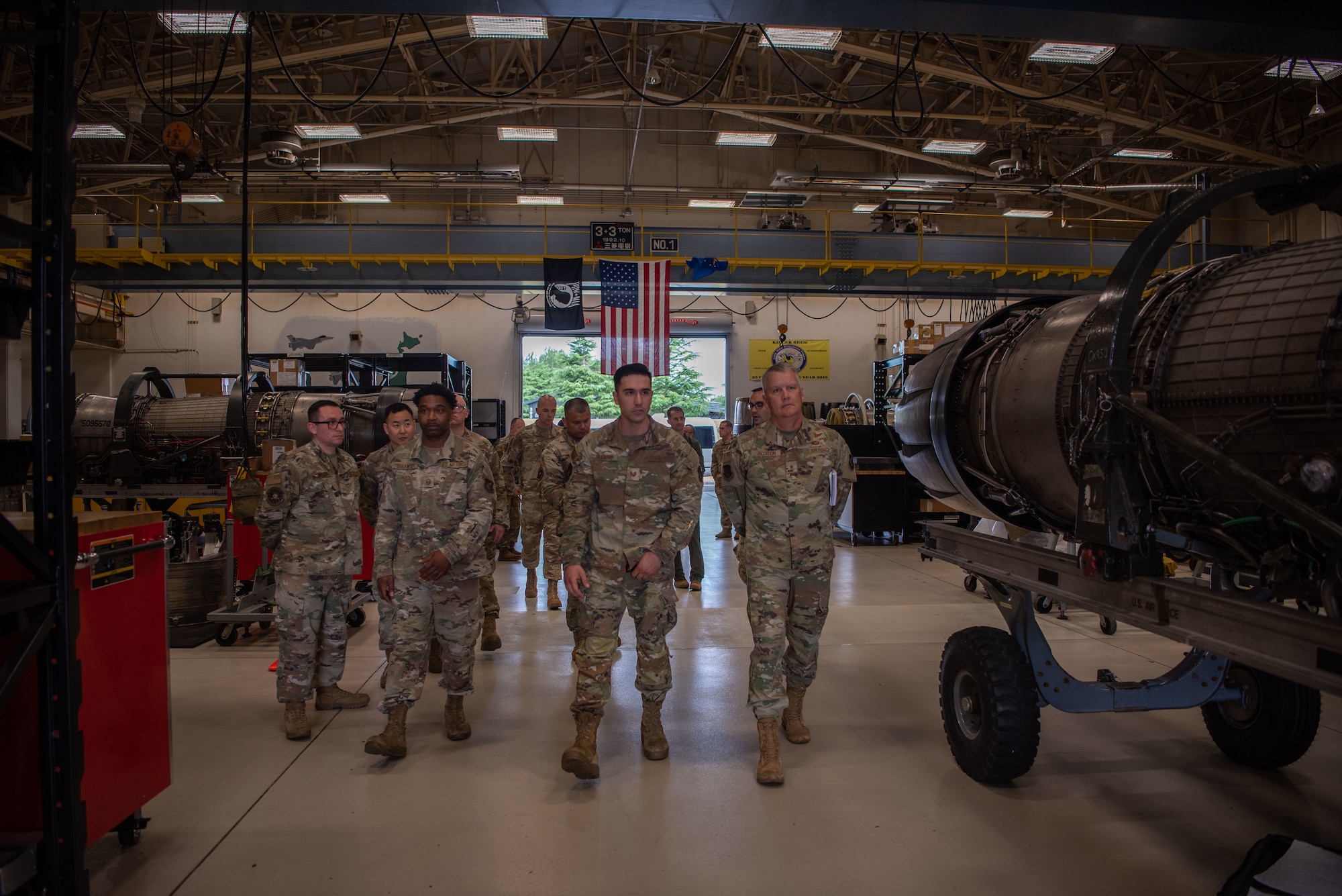 U.S. military members in uniform walk through a hanger working on F-16 Fighting Falcon engines.
