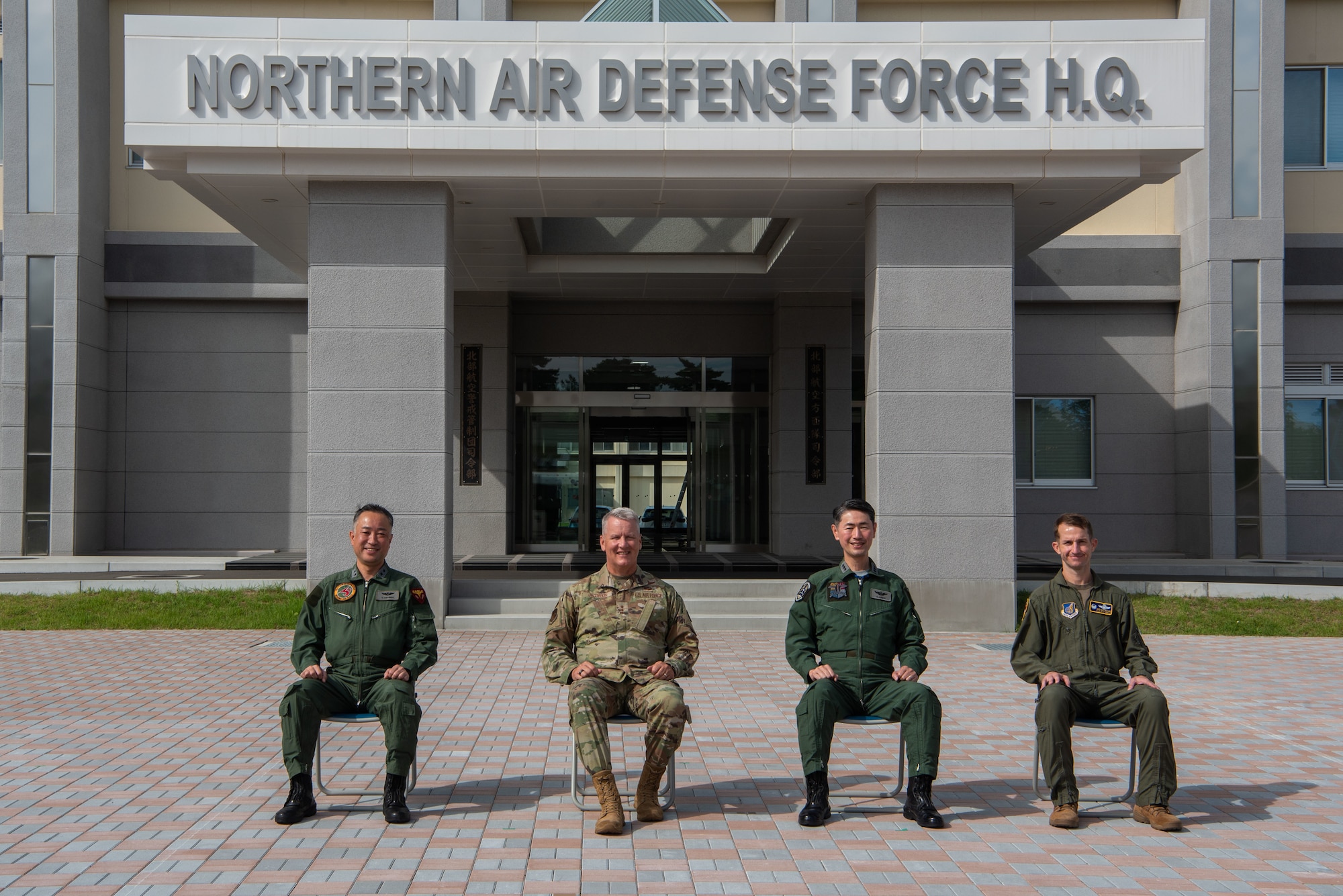 U.S. and Japanese military members sit alongside each other in front of a "Northern Air Defense Force H.Q." sign.
