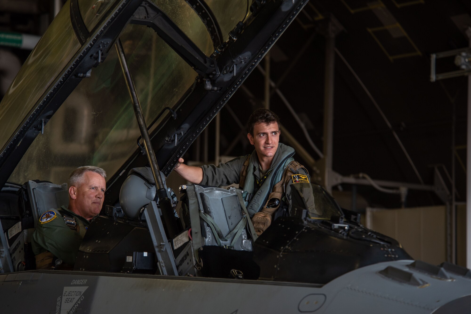 Two military members get into the cockpit of a F-16 Fighting Falcon.