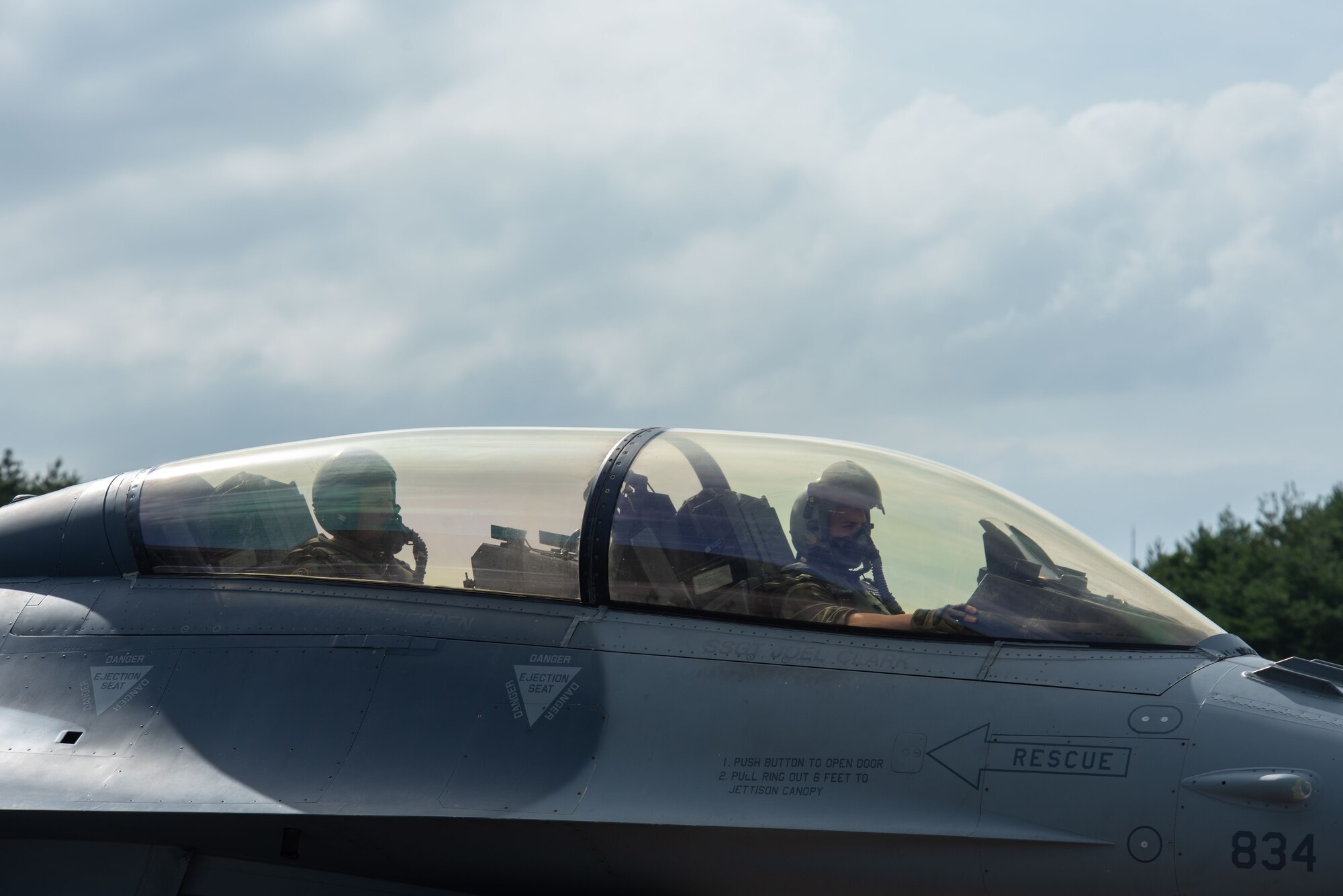 Two military members sit in the cockpit of an F-16 Fighting Falcon.