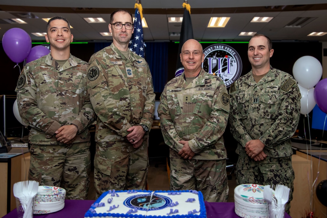 Four military men in uniform pose for a photo in front of a cake