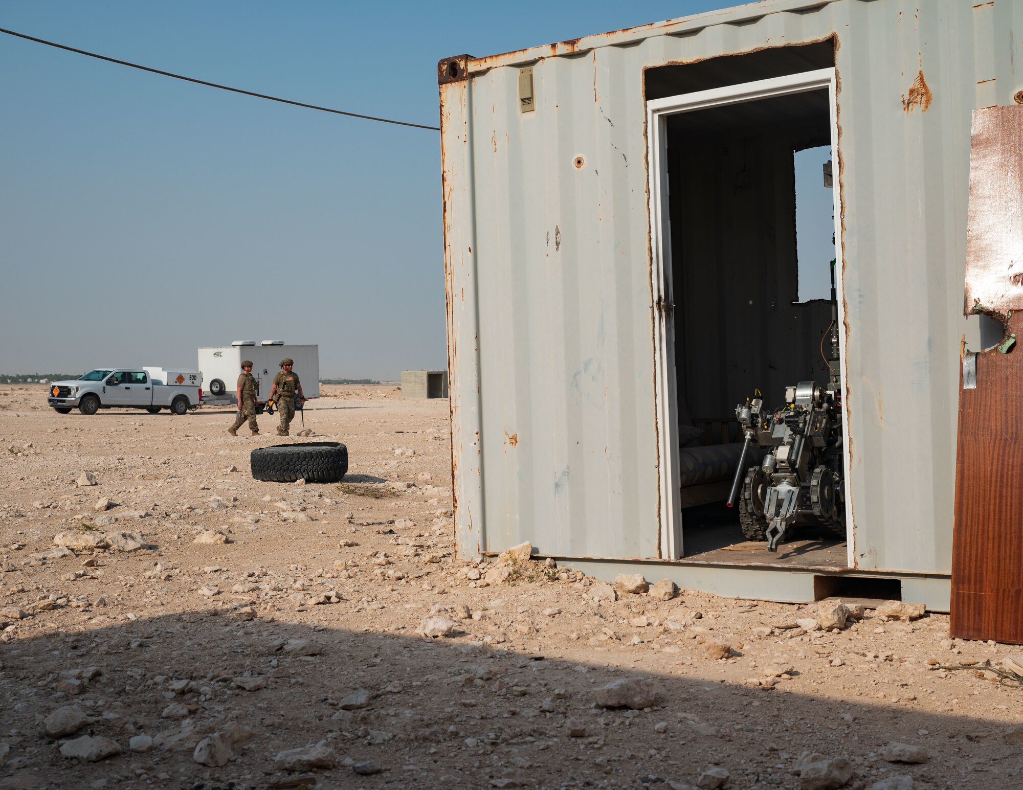 U.S. Air Force Staff Sgts. Cory Lessard and Daniel Simmons, Explosive Ordnance Disposal technicians from 379th Expeditionary Civil Engineer Squadron, approach the simulated explosion zone during an exercise Aug. 24, 2022 at Al Udeid Air Base, Qatar. The robot in the foreground allowed for Lessard and Simmons to examine and evaluate the threat level of the explosion zone from a safe distance prior to making their approach. (U.S. Air Force photo by Staff Sgt. Dana Tourtellotte)