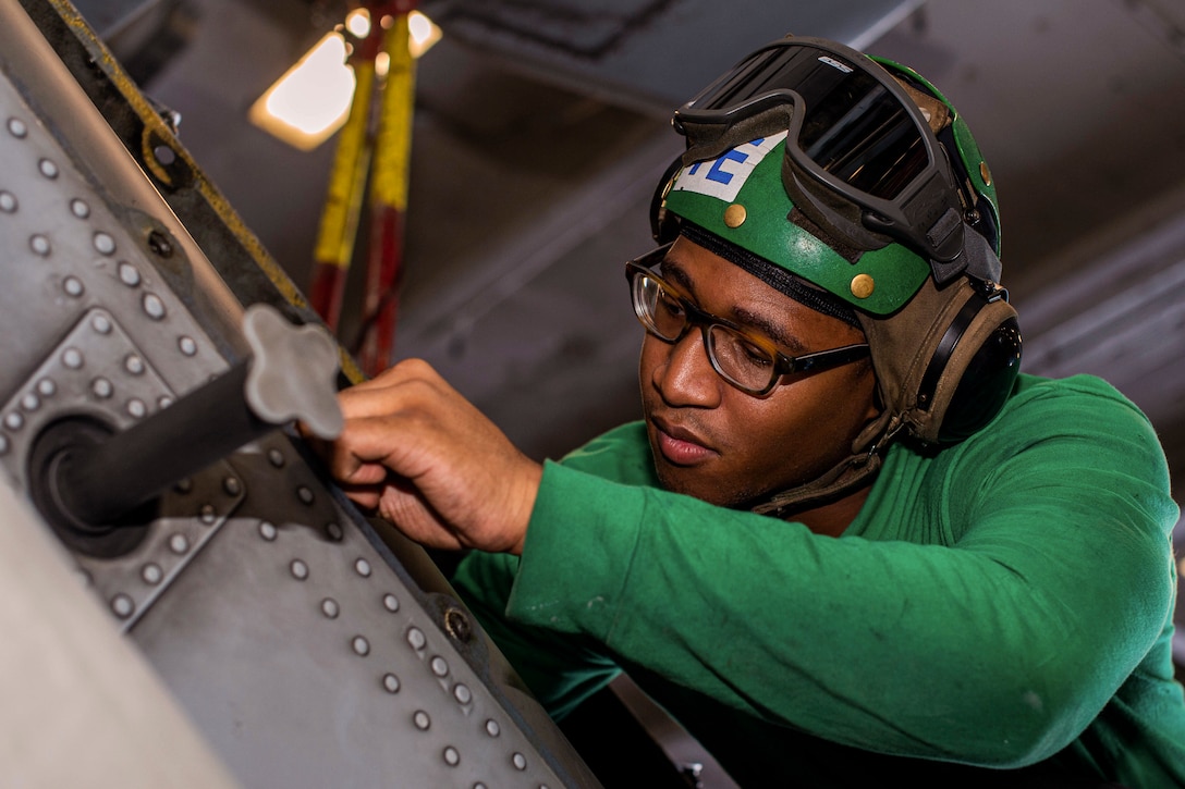 A sailor wearing protective gear works on a helicopter aboard a ship at sea.