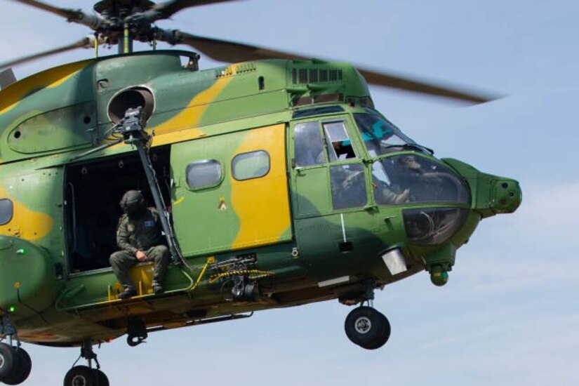 A service members sits in the doorway of an airborne helicopter.