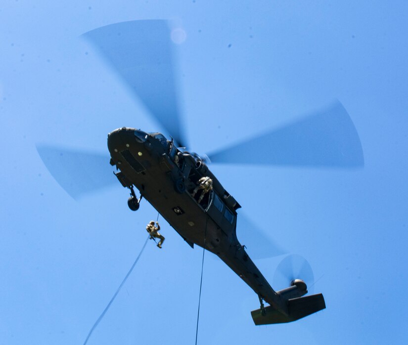A soldier rappels down a rope attached to an airborne helicopter.