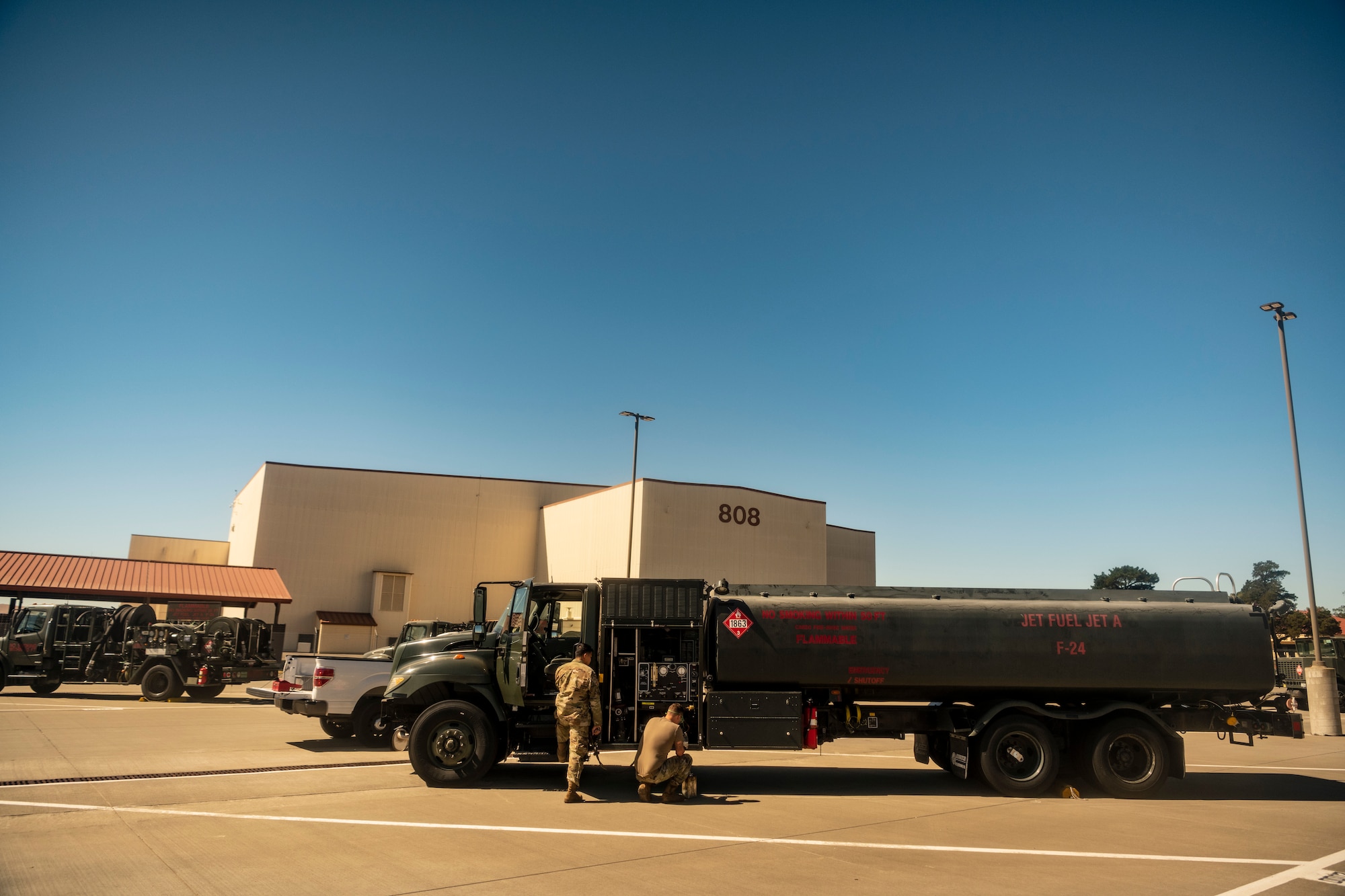 men do service on a large green truck with a huge gas tank on the back