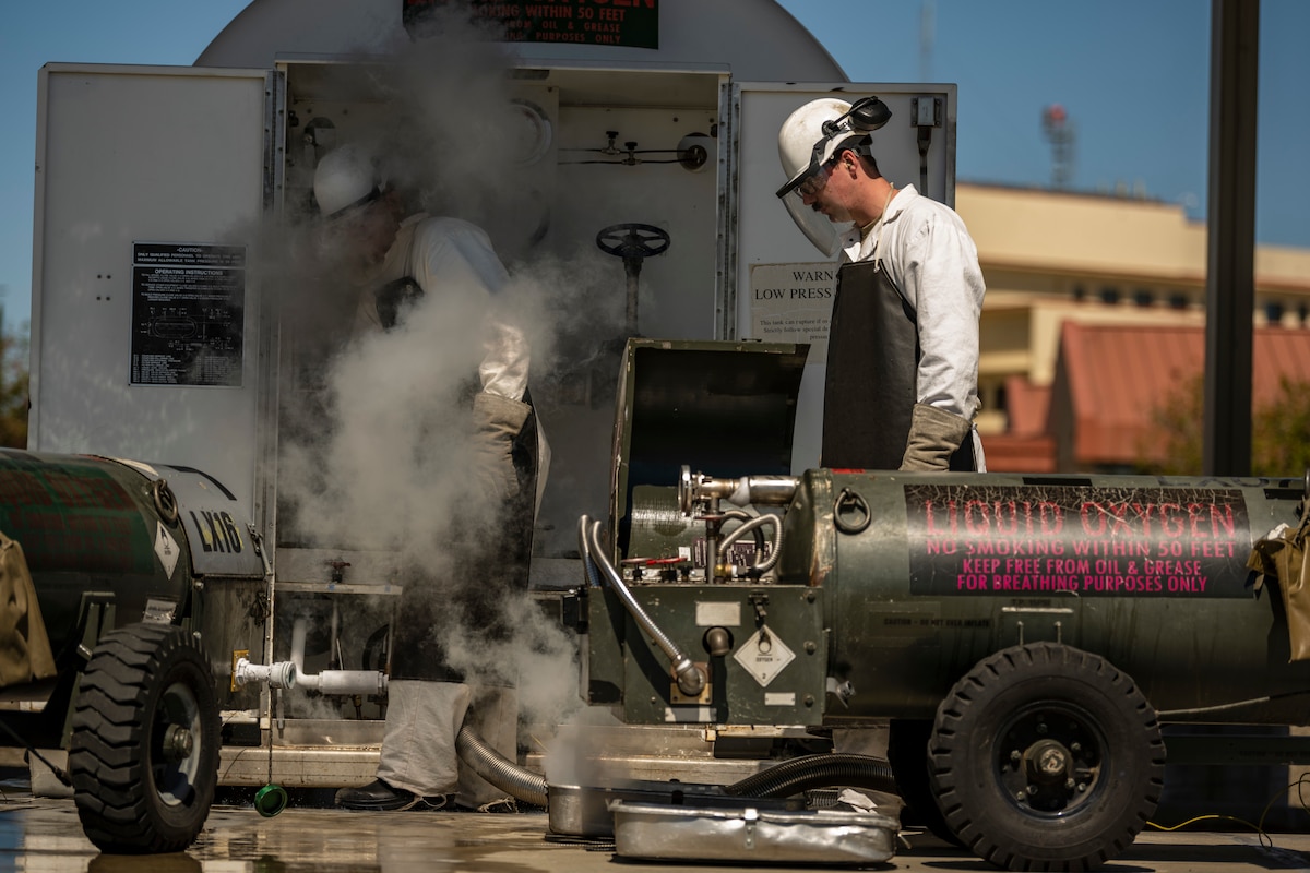 two men in a lot of personal protective equipment work around liquid oxygen