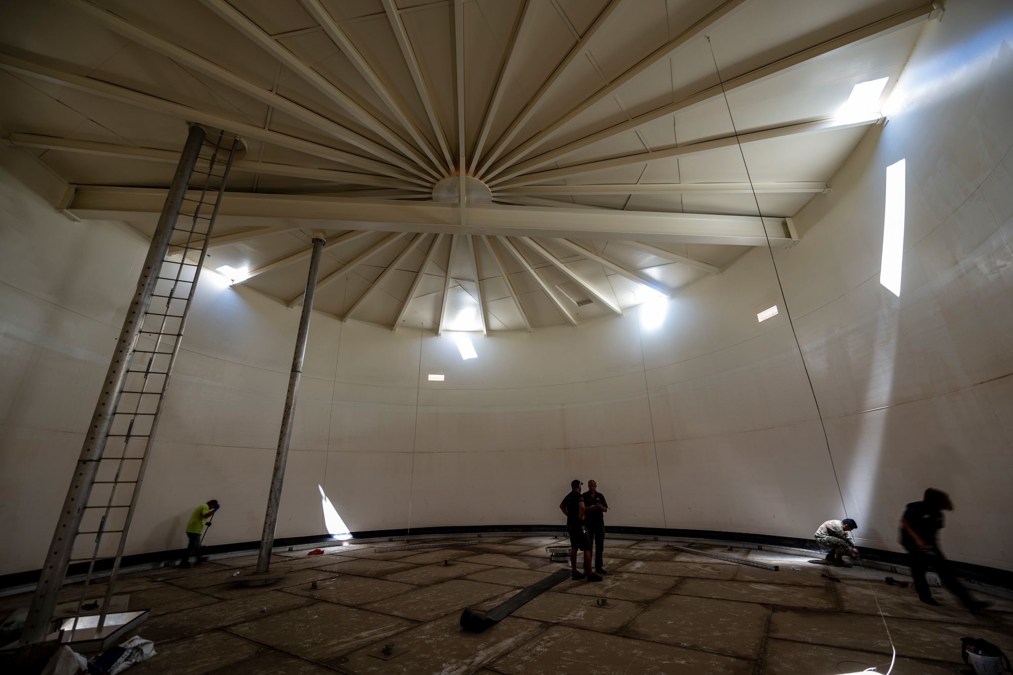 men do work inside a massive tan empty storage tank