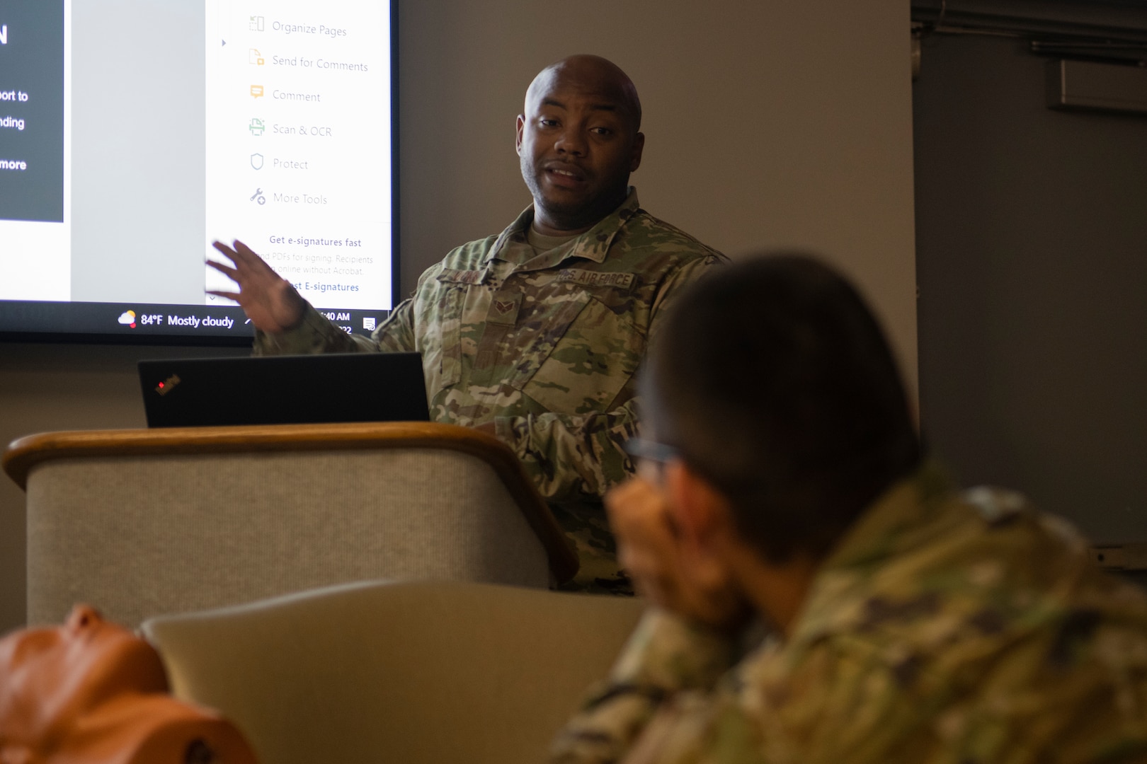 A service member stands at a podium to address other service members.