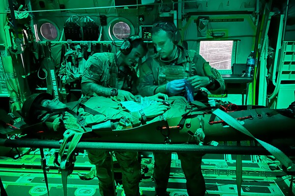 Two service members talk as they stand over a patient.