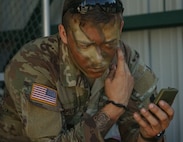 A Soldier from the Headquarters and Headquarters Company, 1st Battalion, 110th Infantry Regiment, 2nd Infantry Brigade Combat Team, applies camouflage before the scout Soldiers move onto their training mission at Fort Indiantown Gap, Pa., on August 3, 2022. The scout Soldiers developed their abilities to communicate and asses as they moved into the woods on their mission (U.S Army photo by Sgt. 1st Class Matthew Keeler)
