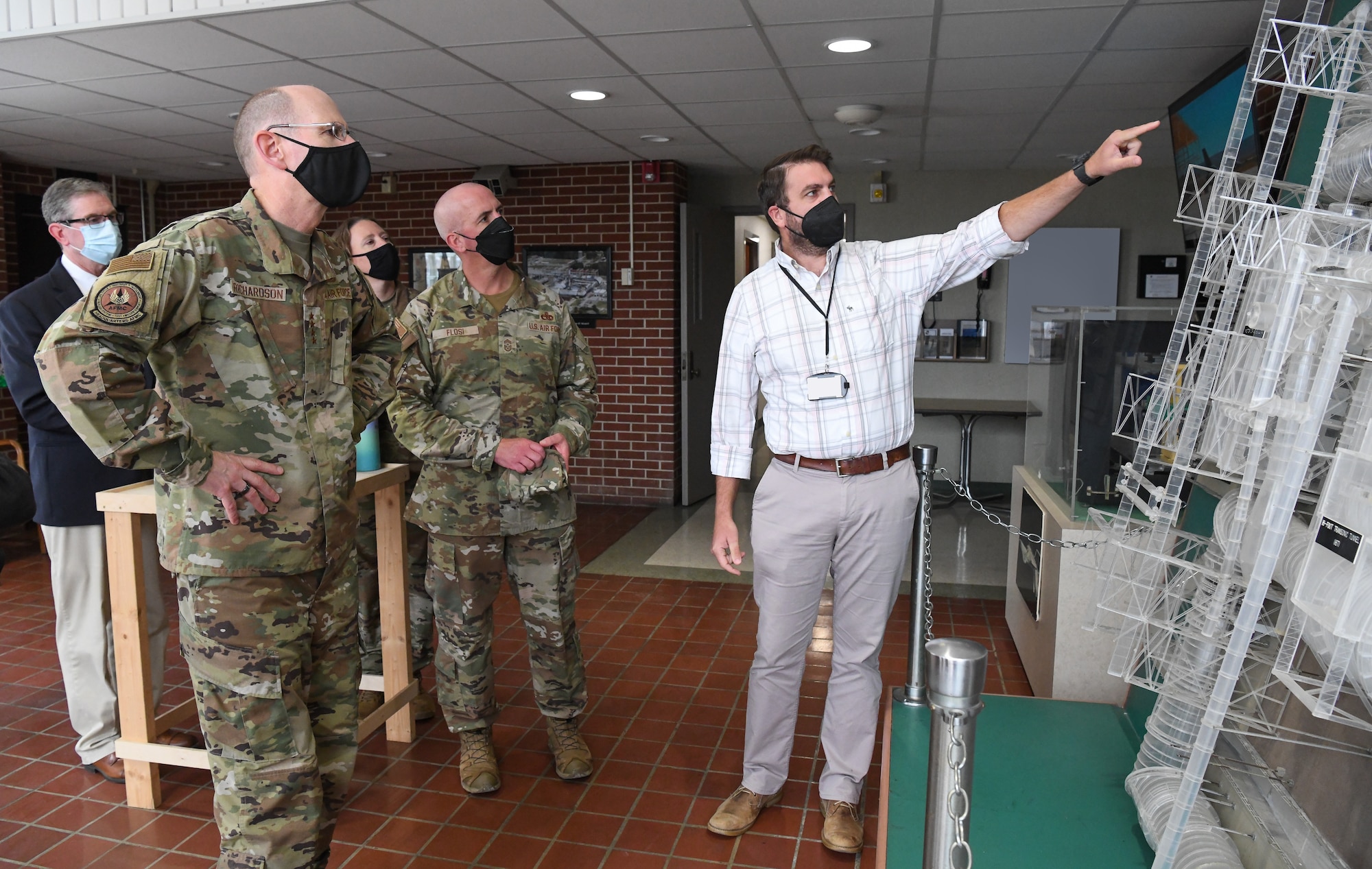 Civilian employee points to a model as others look on