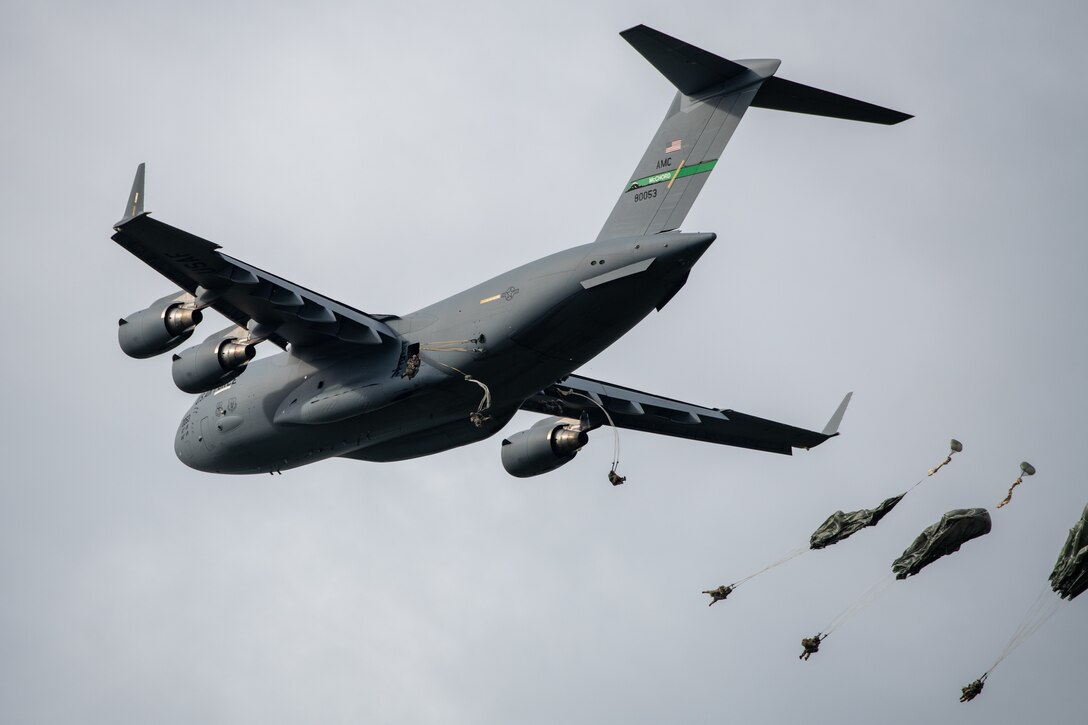 Paratroopers leap from a C-17 aircraft.