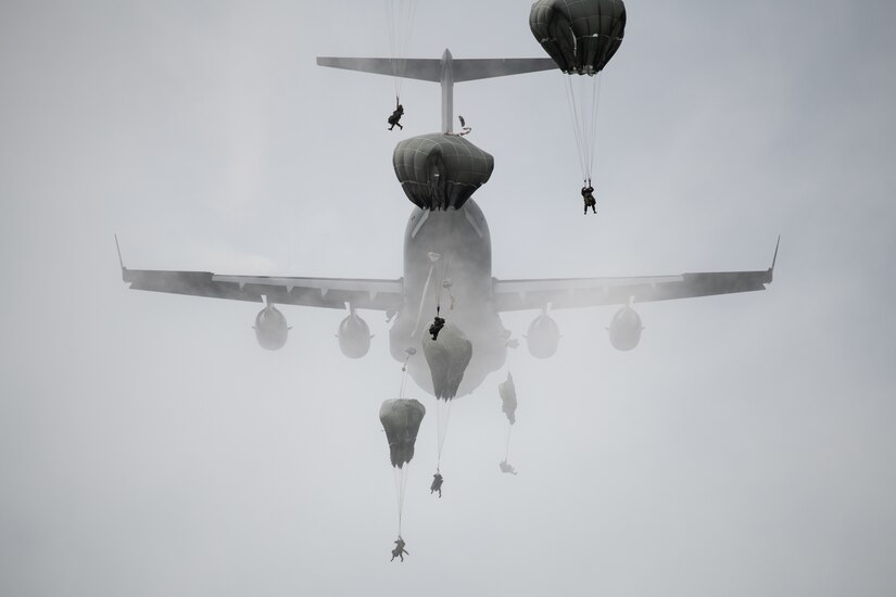 Paratroopers leap from a C-17 aircraft.