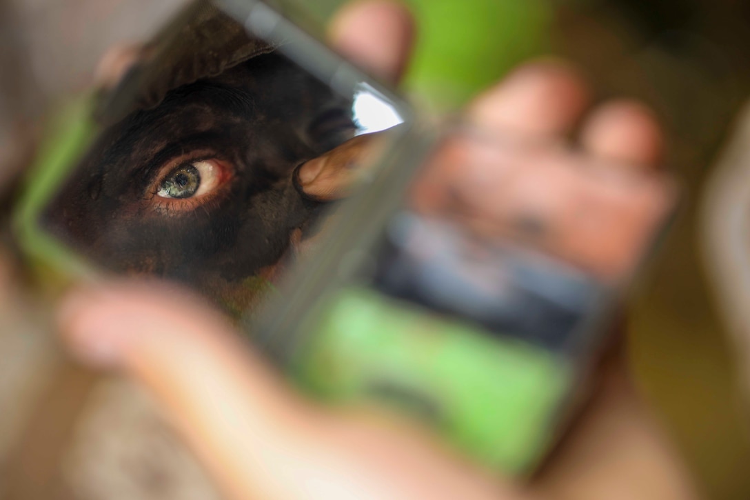 A recruit applies camouflage face paint while looking in a mirror.