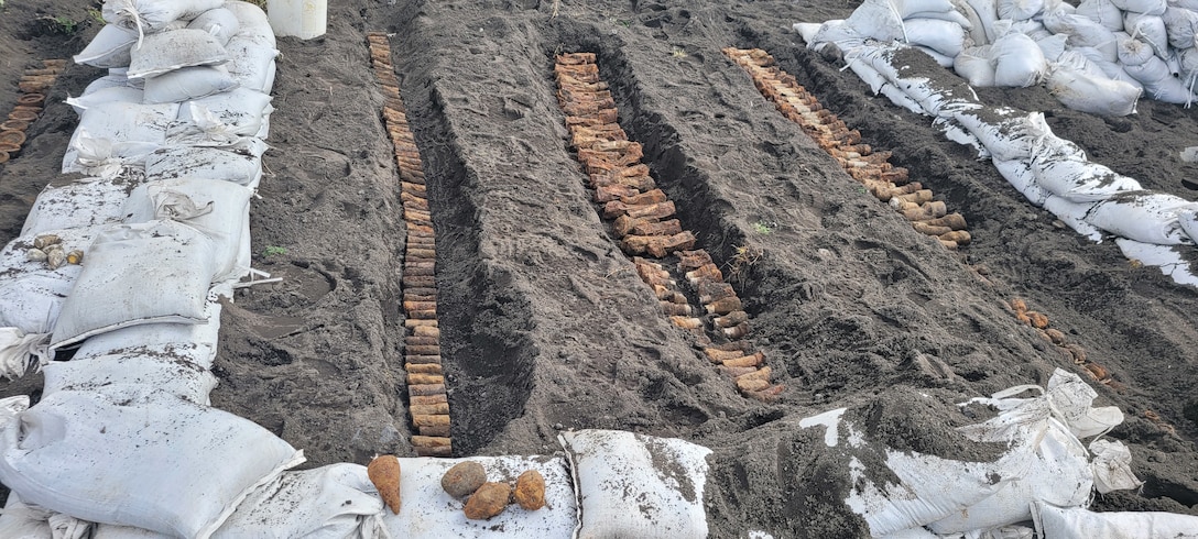 A field crew for the U.S. Army Corps of Engineers placed recovered military munitions in trenches at the Fort Glenn Formerly Used Defense Site on Umnak Island in Alaska. Technicians used controlled explosions to safely dispose of the consolidated piles of ordnance. (U.S. Army Photo)