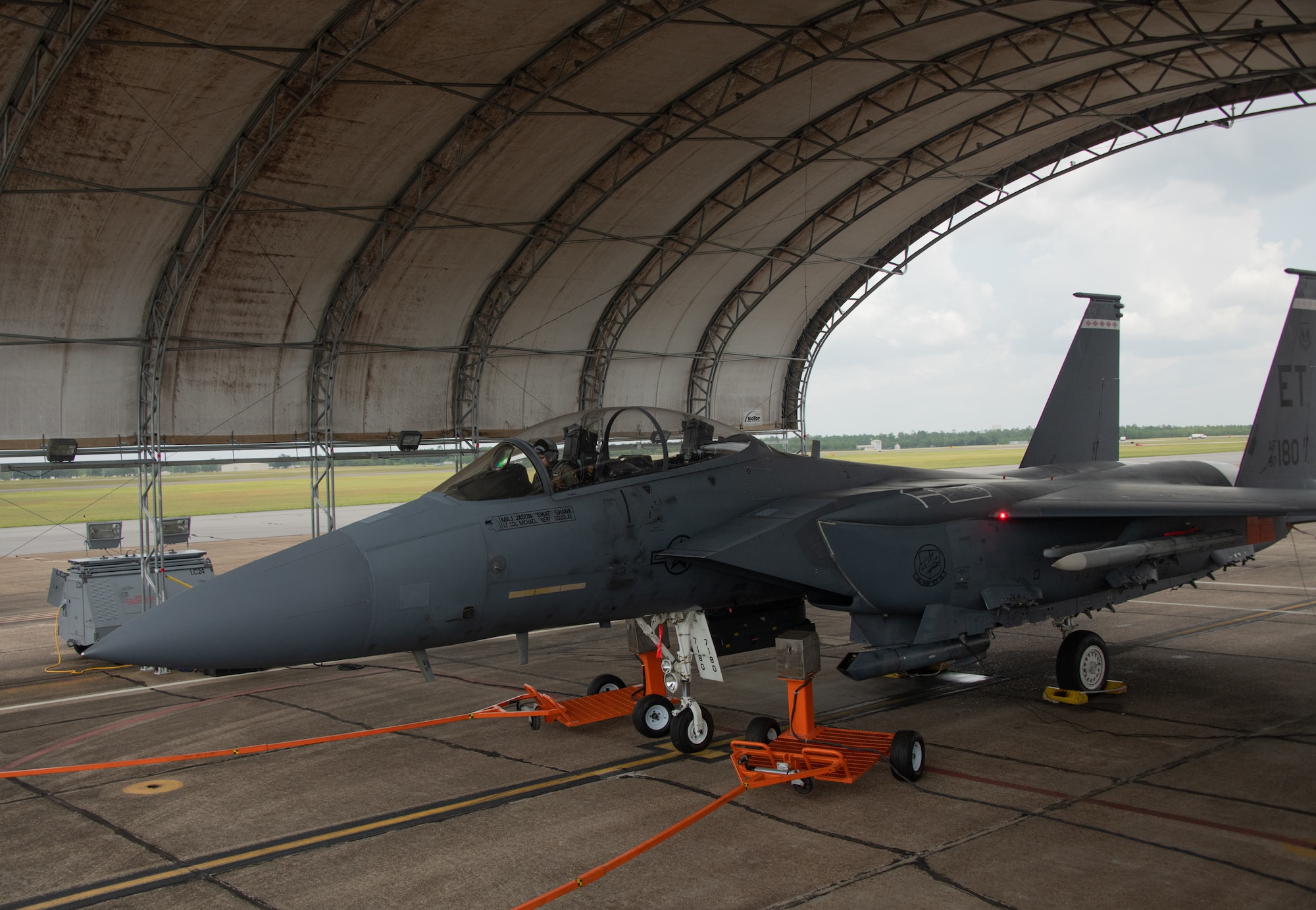 Analysts from the Air Force Research Laboratory's 711th Human Performance Wing use the orange spray carts displayed to insert oil of wintergreen into the idling F-15E Strike Eagle prior to taxi at Eglin Air Force Base, Fla., Aug. 16, 2022. This test is part of a larger Department of Defense effort to evaluate cockpit environmental conditions after a chemical weapon attack (U.S. Air Force photo by Ilka Cole)