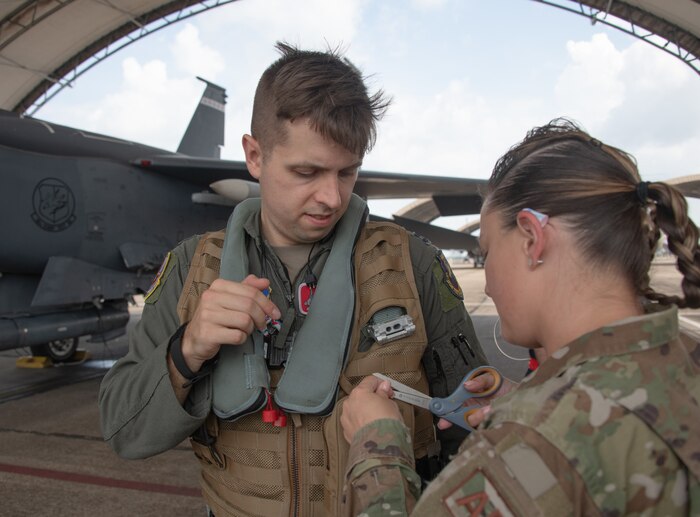 An Aircrew Flight Equipment member secures the zippers on the pilot's vest radio pouch prior to flight in accordance with operational procedures. Securing the pouch zippers ensures that the test sensor remains secure in the event that the pilot would need to eject from the aircraft at Eglin Air Force Base, Fla., Aug.16, 2022. The equipment in the radio pouch provides valuable data to aircraft design teams and opportunities to enhance aircraft environments and improve aircrew equipment.  (U.S. Air Force photo by Ilka Cole)