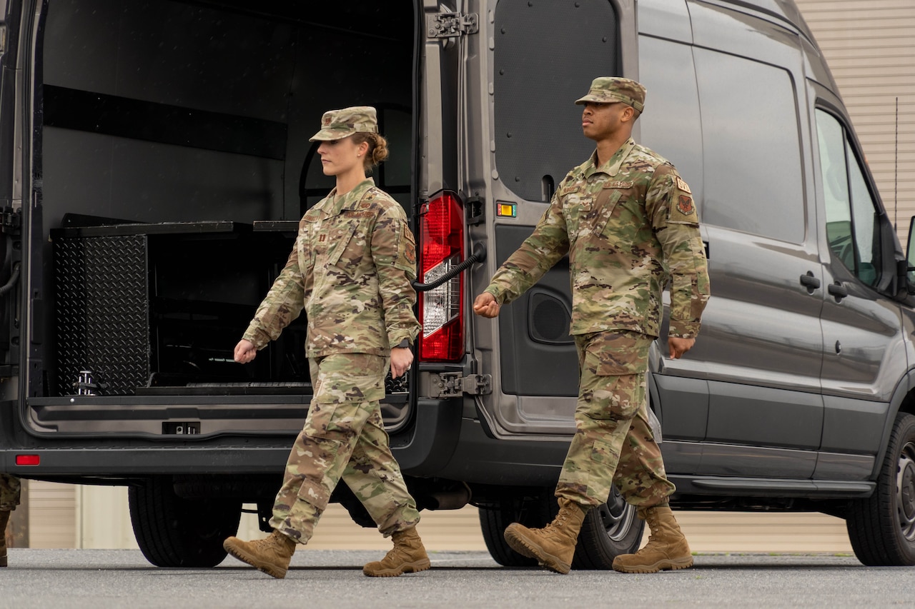 Two airmen walk near the back of an open van.