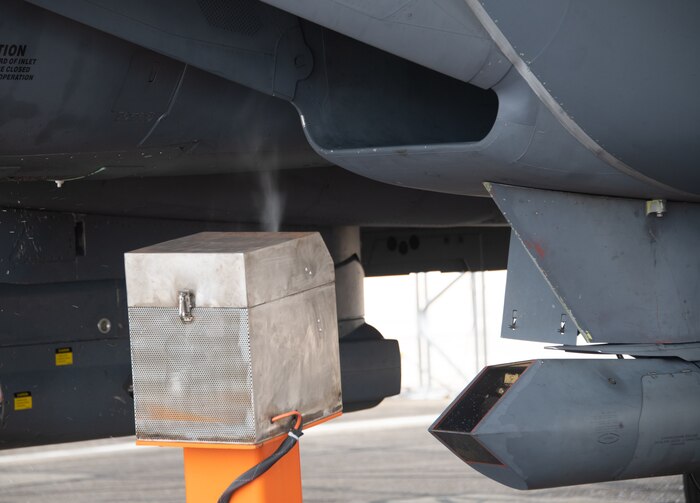 Analysts from the Air Force Research Laboratory's 711th Human Performance Wing use the orange spray carts displayed to insert oil of wintergreen into the idling F-15E Strike Eagle prior to taxi at Eglin Air Force Base, Fla., Aug. 16, 2022. This test is part of a larger Department of Defense effort to evaluate cockpit environmental conditions after a chemical weapon attack (U.S. Air Force photo by Ilka Cole)