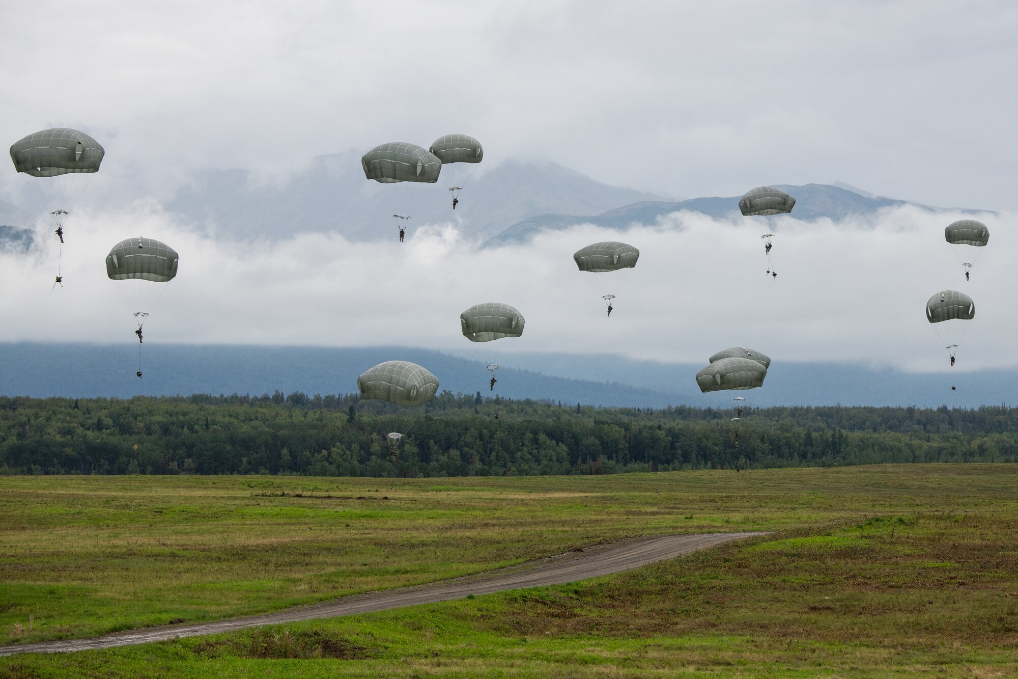Soldiers float down with parachutes in front of a foggy mountain.