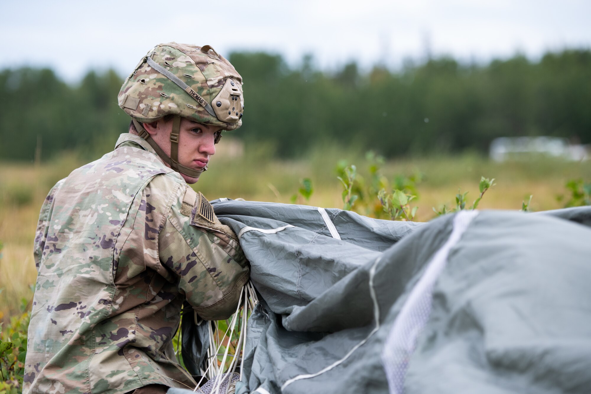 A soldier pulls at his parachute to pack it after airborne operations.